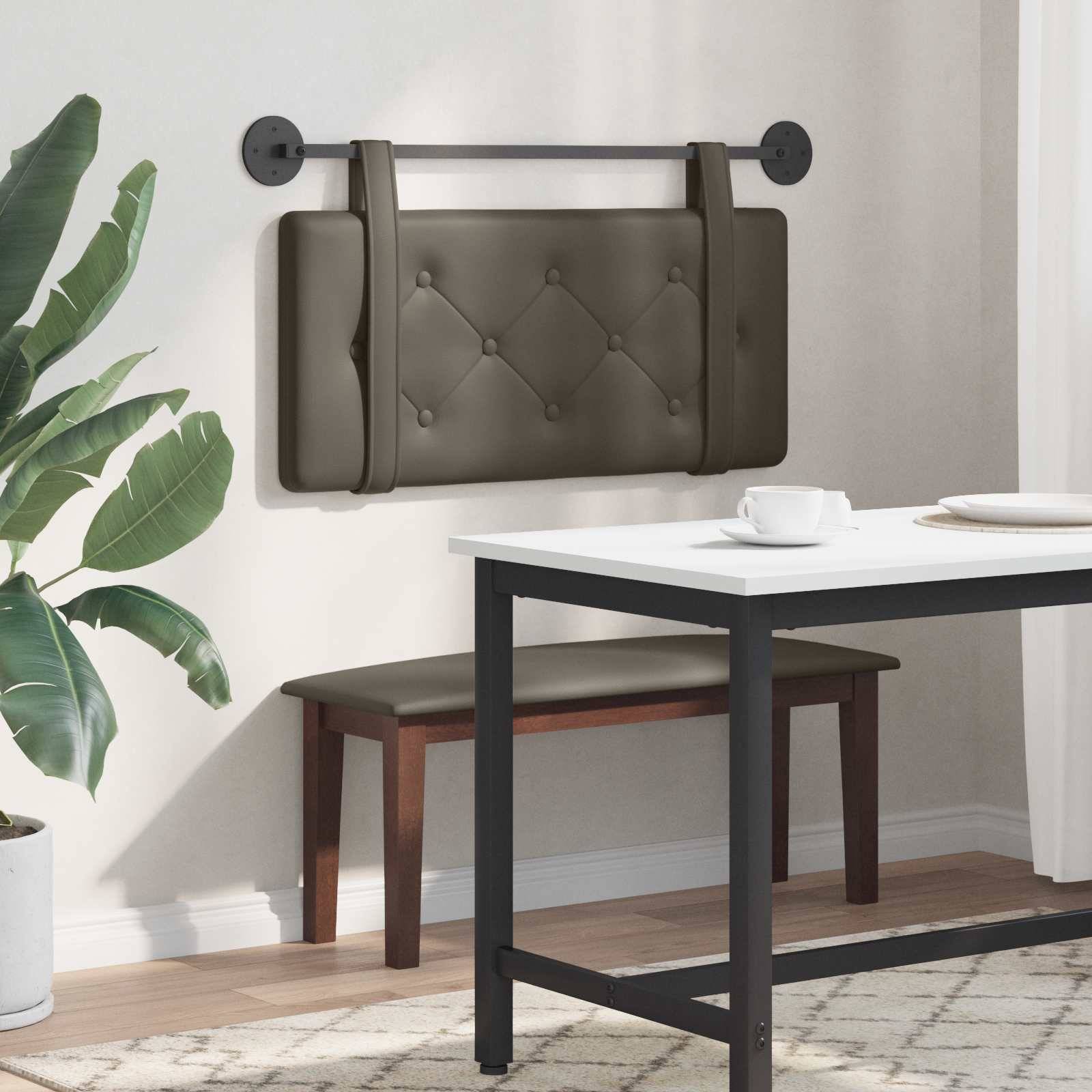 Eine schmale, gepolsterte Bank mit gestepptem Design ist an einer Wand neben einem weißen Tisch und Stuhl angebracht. Eine Topfpflanze befindet sich in der Nähe.