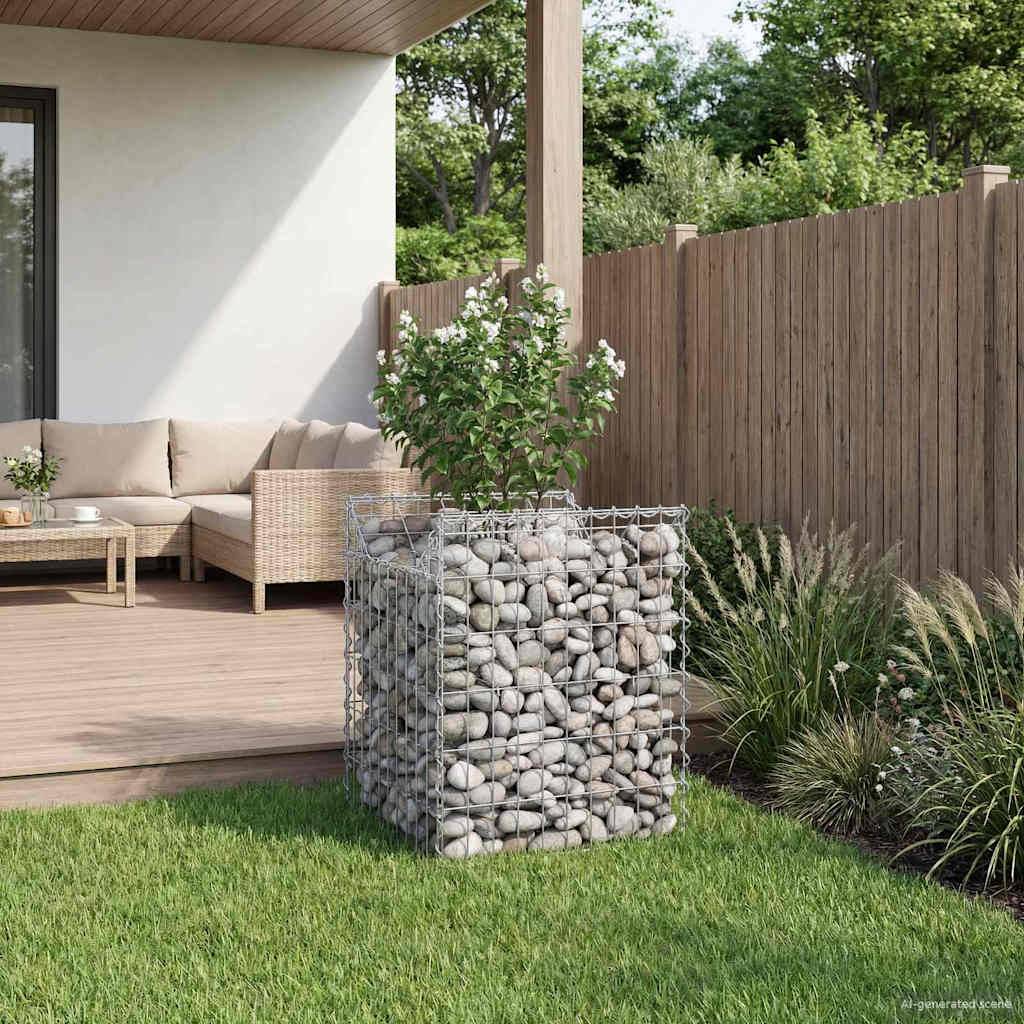 Eine gemütliche Terrasse mit einem Holzdeck bietet ein bequemes Sofa, einen kleinen Tisch und einen mit Steinen gefüllten Pflanzkübel. Ein Holzzaun und Grün umgeben den Bereich.