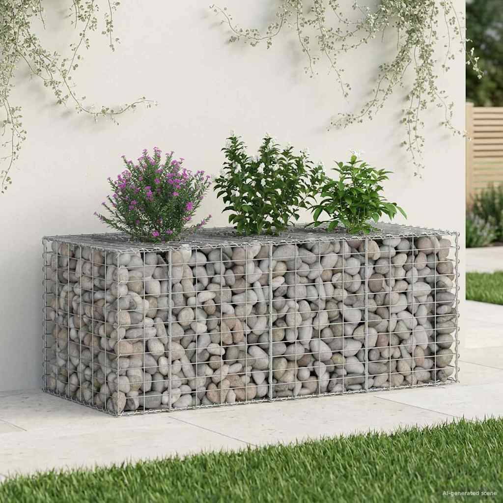 Ein mit Steinen gefüllter Gabionen-Pflanzkübel mit grünen und violetten blühenden Pflanzen, auf einer Terrasse platziert. Kletterpflanzen ergießen sich von oben herab.