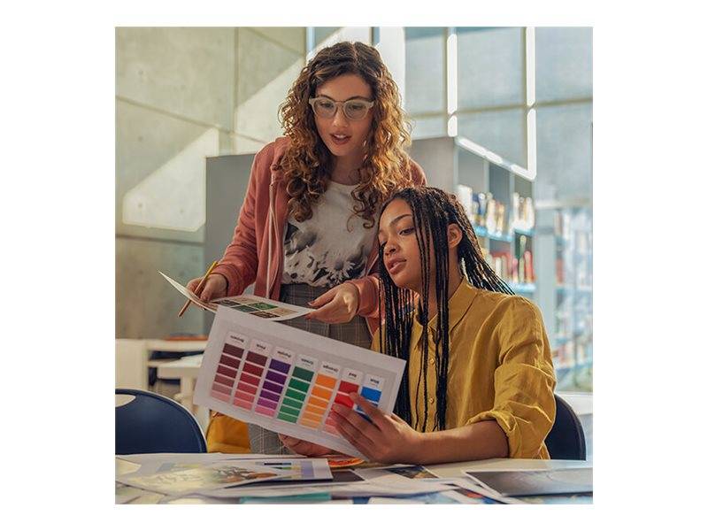 Zwei Frauen überprüfen Farbmuster und Druckmuster an einem Designtisch in einem hellen Studio oder Klassenzimmer.