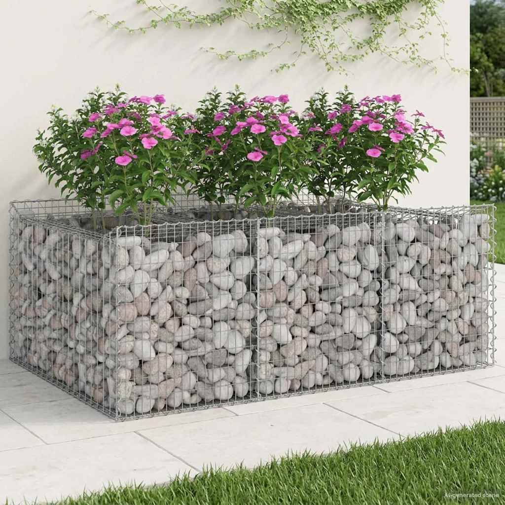Ein rechteckiger, mit Steinen gefüllter Drahtgabionen-Pflanzbehälter hält rosa Blüten gegen eine hellgefärbte Mauer mit Kletterpflanzen.