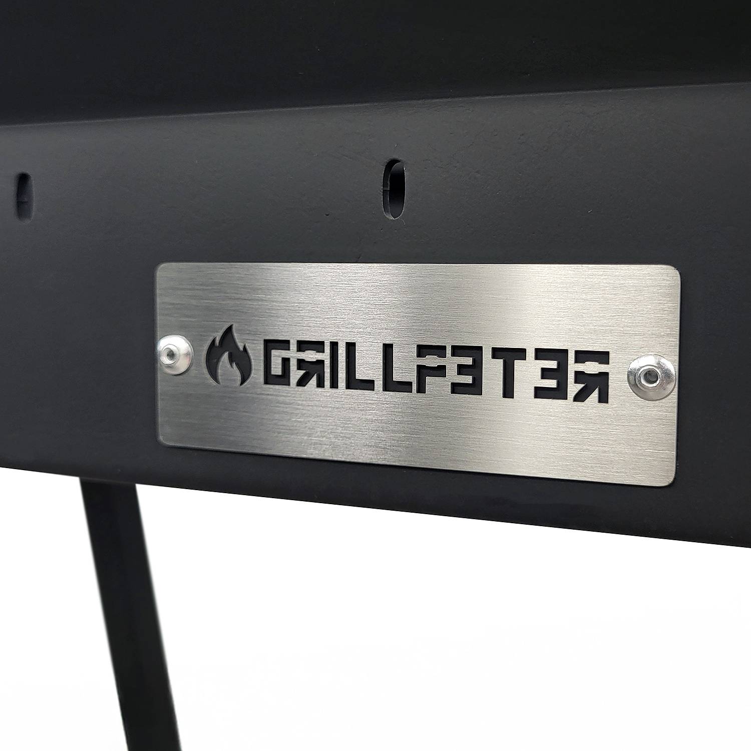 Metallschild 'GRILLFATER' mit Flammensymbol auf einem schwarzen Grill- oder Gerätepaneel.