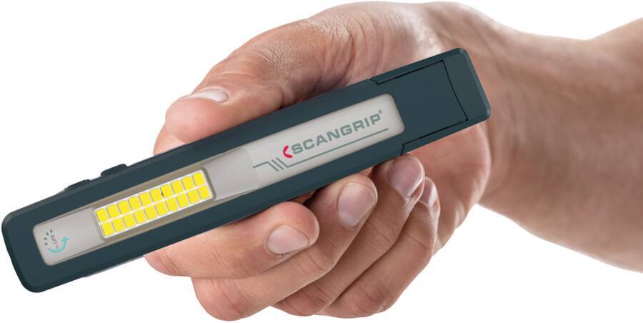 Eine Hand hält eine Scangrip LED-Inspektionsleuchte, eine schlanke rechteckige Arbeitsleuchte mit gelben LEDs an der Vorderseite.