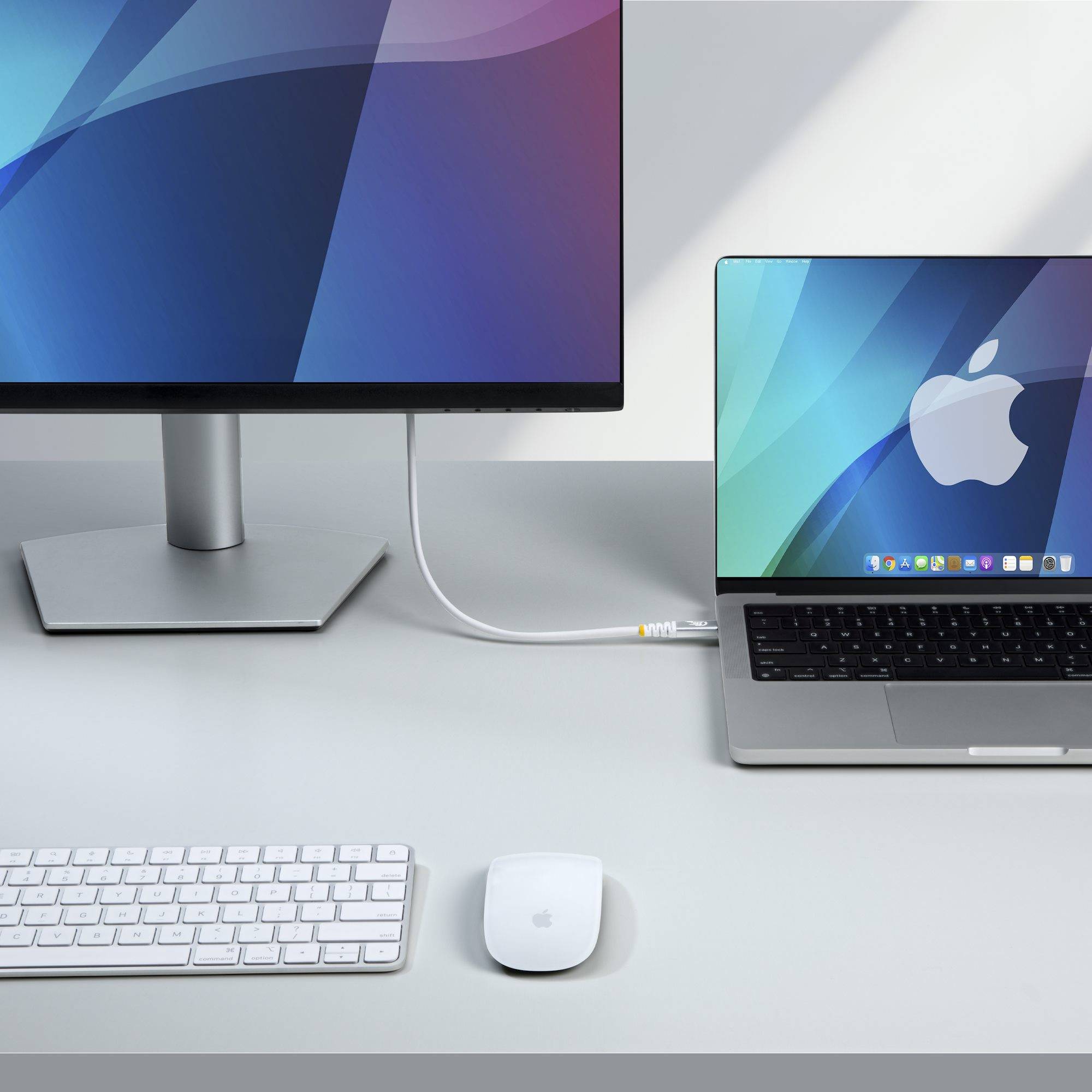 Minimales Apple-Desktop-Setup mit externem Monitor, MacBook, Tastatur und Maus auf einem weißen Schreibtisch.