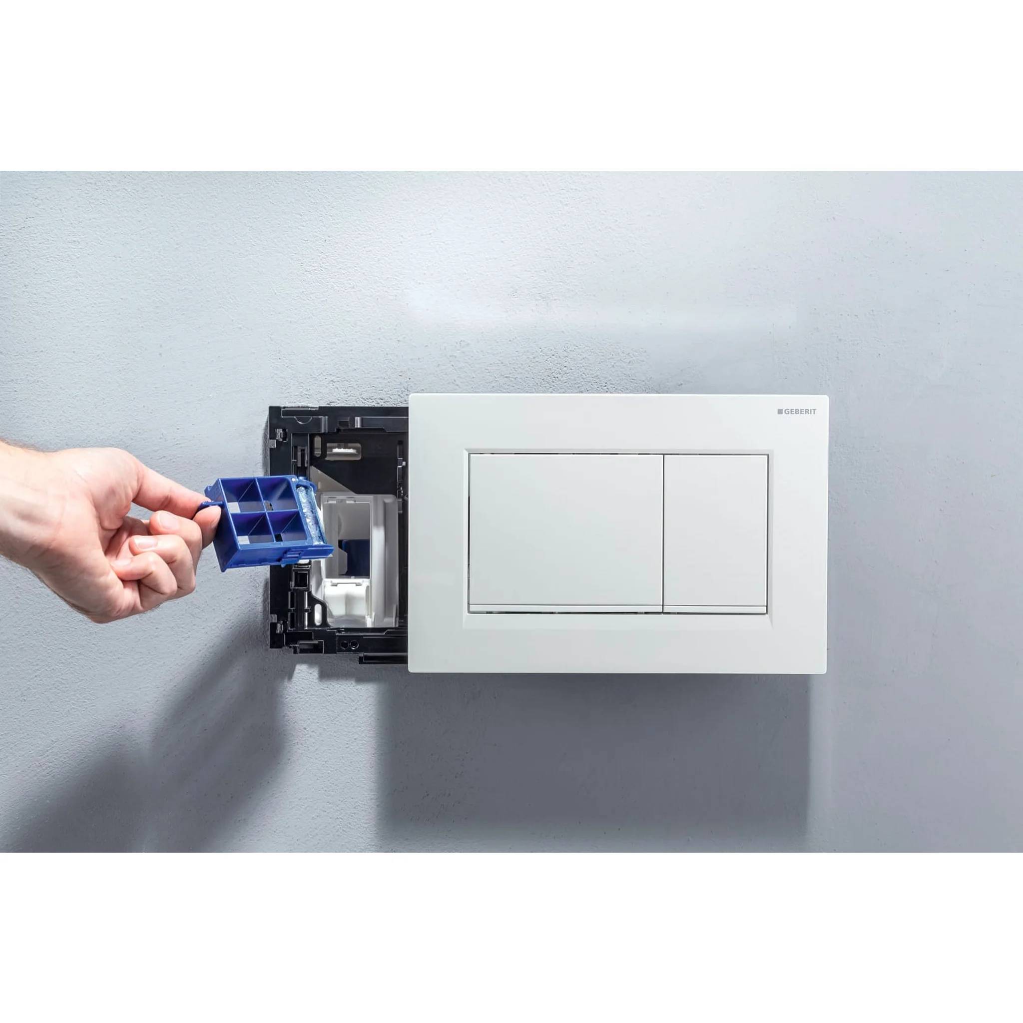 Hand, die eine blaue Schalterkomponente in eine wandmontierte Elektroschalterbox an einer grauen Wand einführt.