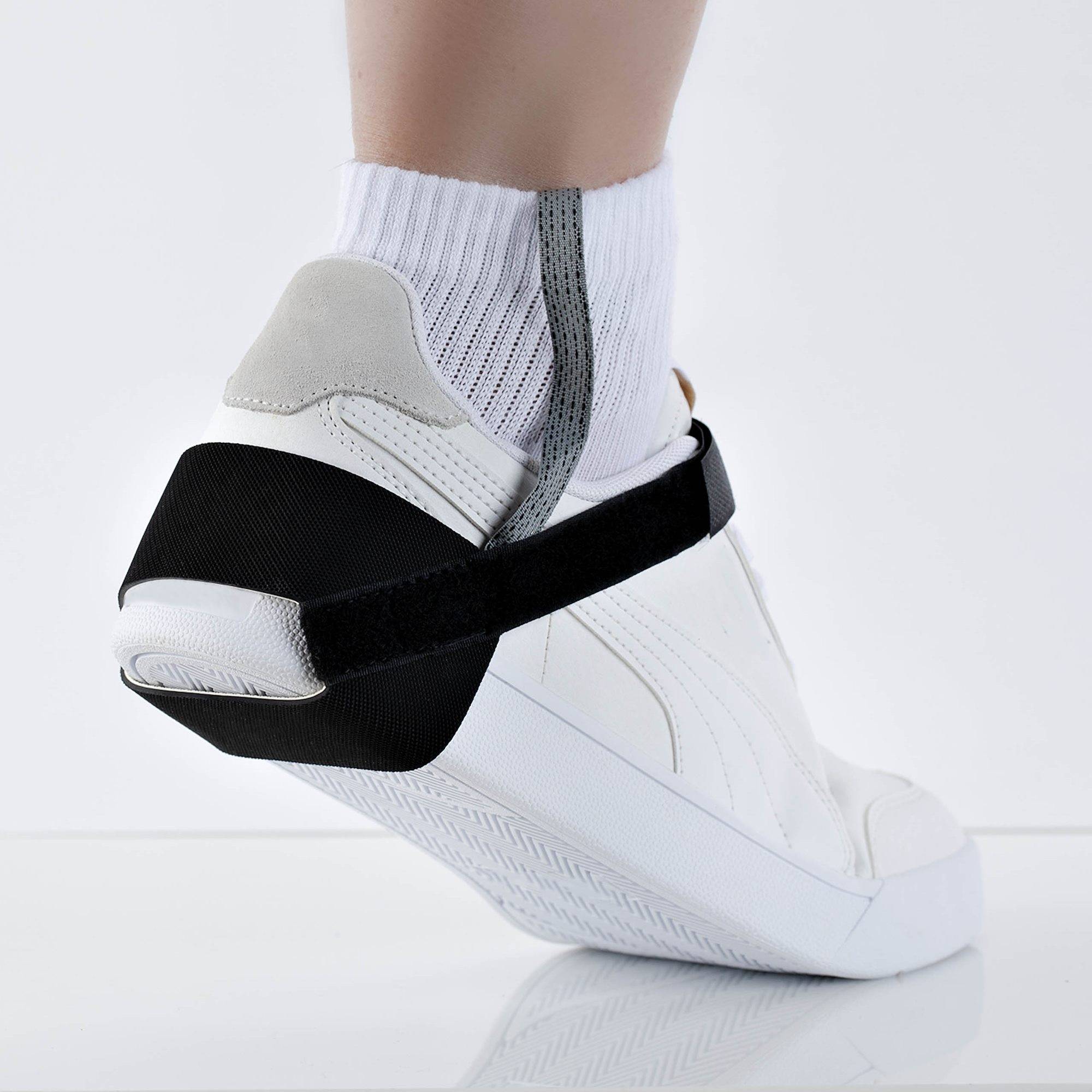 Weiße orthopädische Fußgelenkschiene mit schwarzen Riemen, getragen über einer weißen Socke an einem Fuß, gezeigt in der Seitenansicht auf einem einfachen hellen Hintergrund.