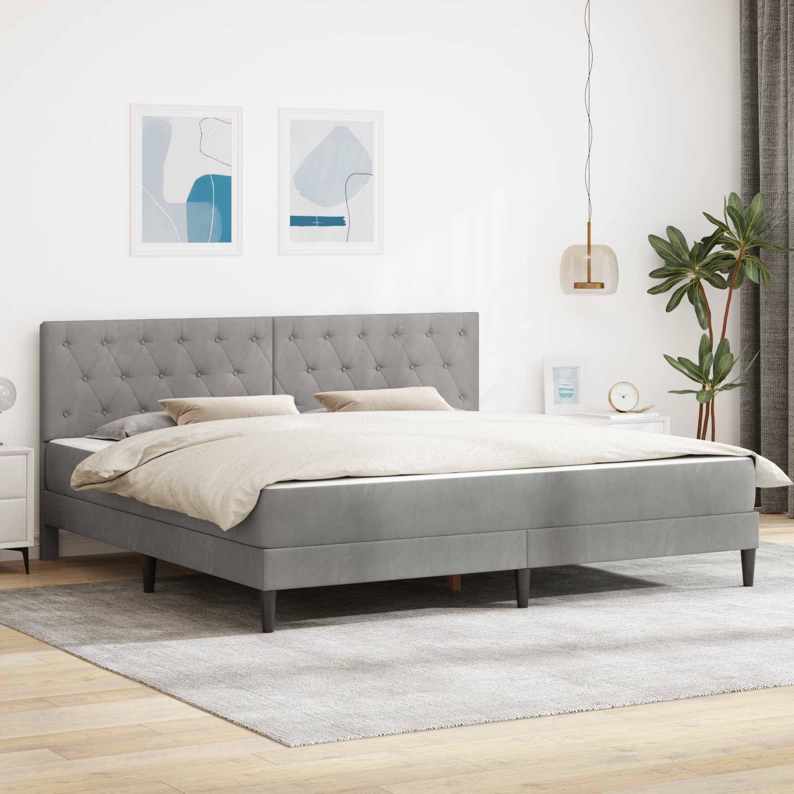 Modernes Schlafzimmer mit grauem Polsterbett, beigem Bedding, Wandkunst, Pendelleuchte und Topfpflanze auf hellem Teppich.