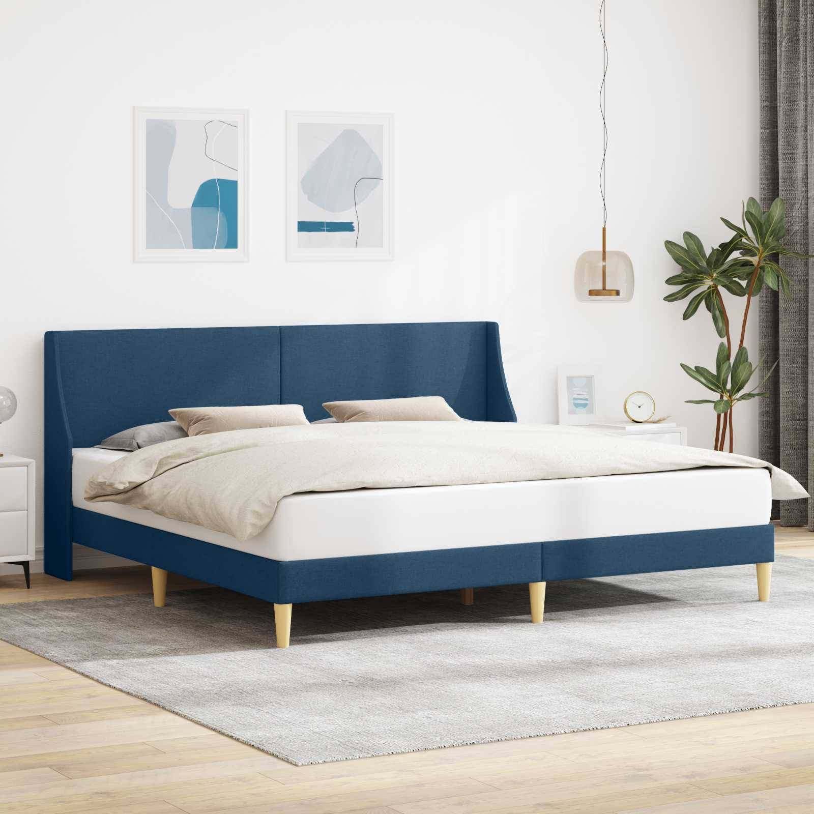 Modernes Schlafzimmer mit einem blau gepolsterten Bett, cremefarbener Bettwäsche, gerahmter Wandkunst, Pendelleuchte, Topfpflanze und hellem Teppich auf Holzboden.