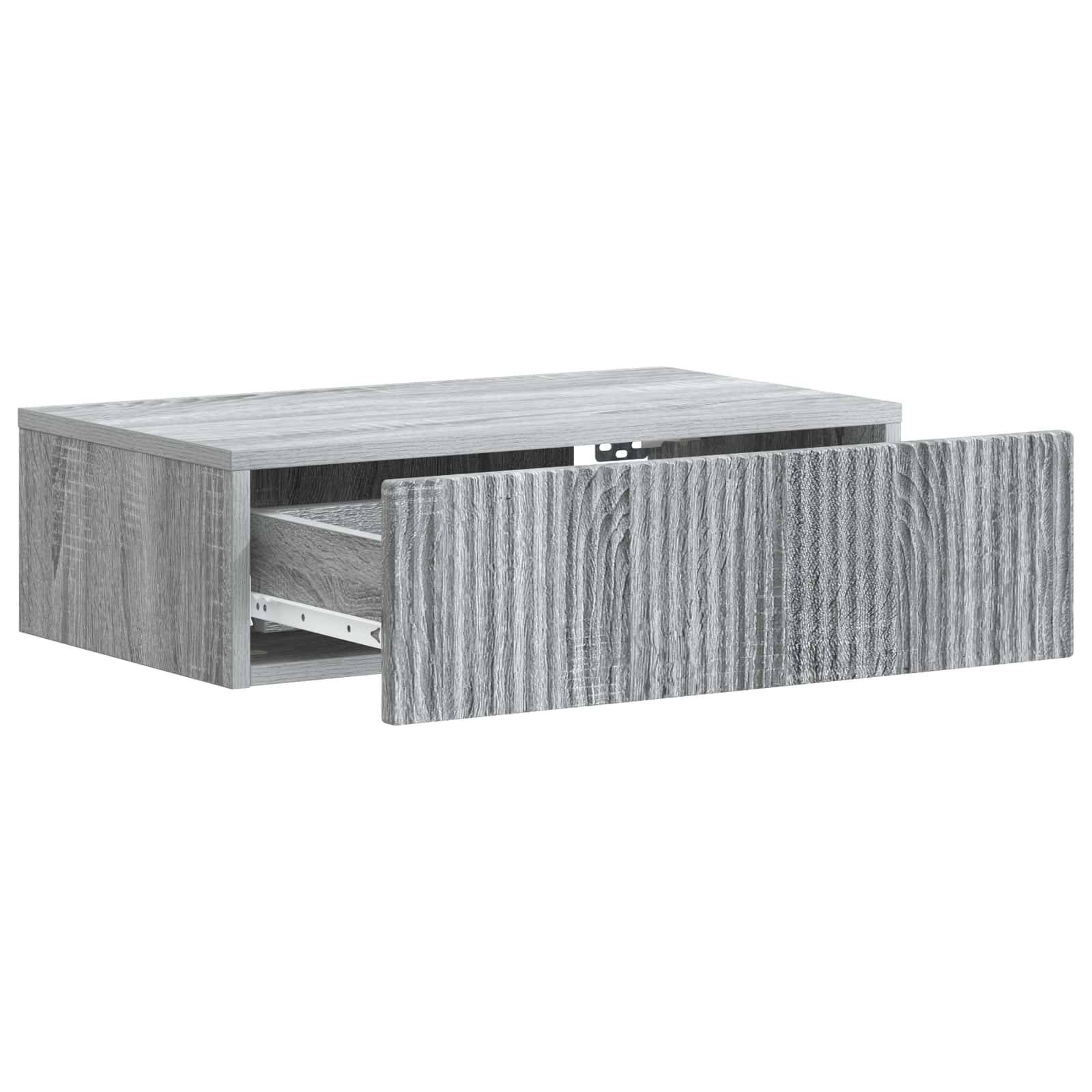 Grauer Schubladenkasten mit Holzmaserung, teilweise geöffnet an einem kleinen Schrank oder Nachttisch, zeigt innere Lagerfläche und Metallschubladenschienen.