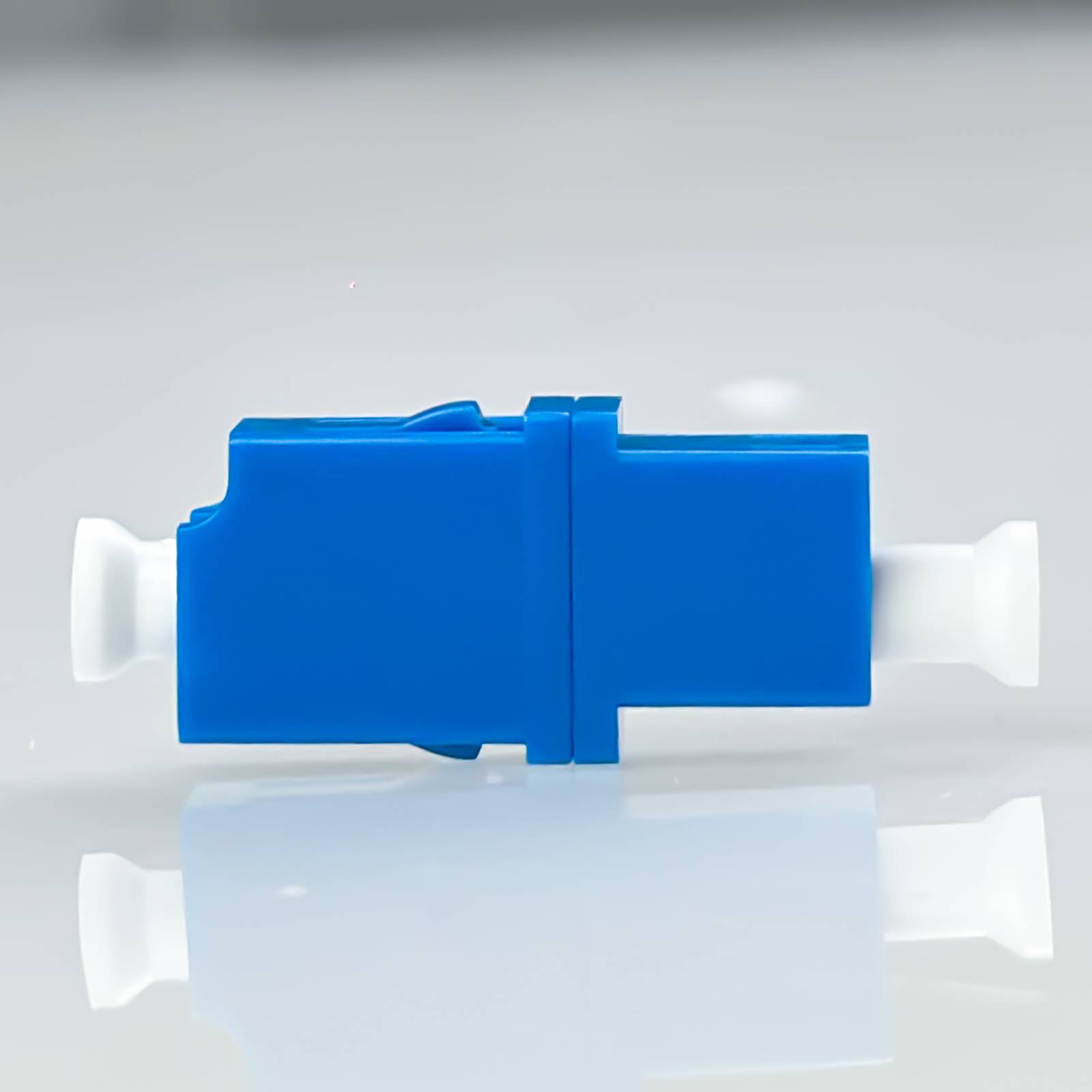 Blau-weißer Lichtwellenleiter-Steckeradapter liegt horizontal auf einer reflektierenden Oberfläche.