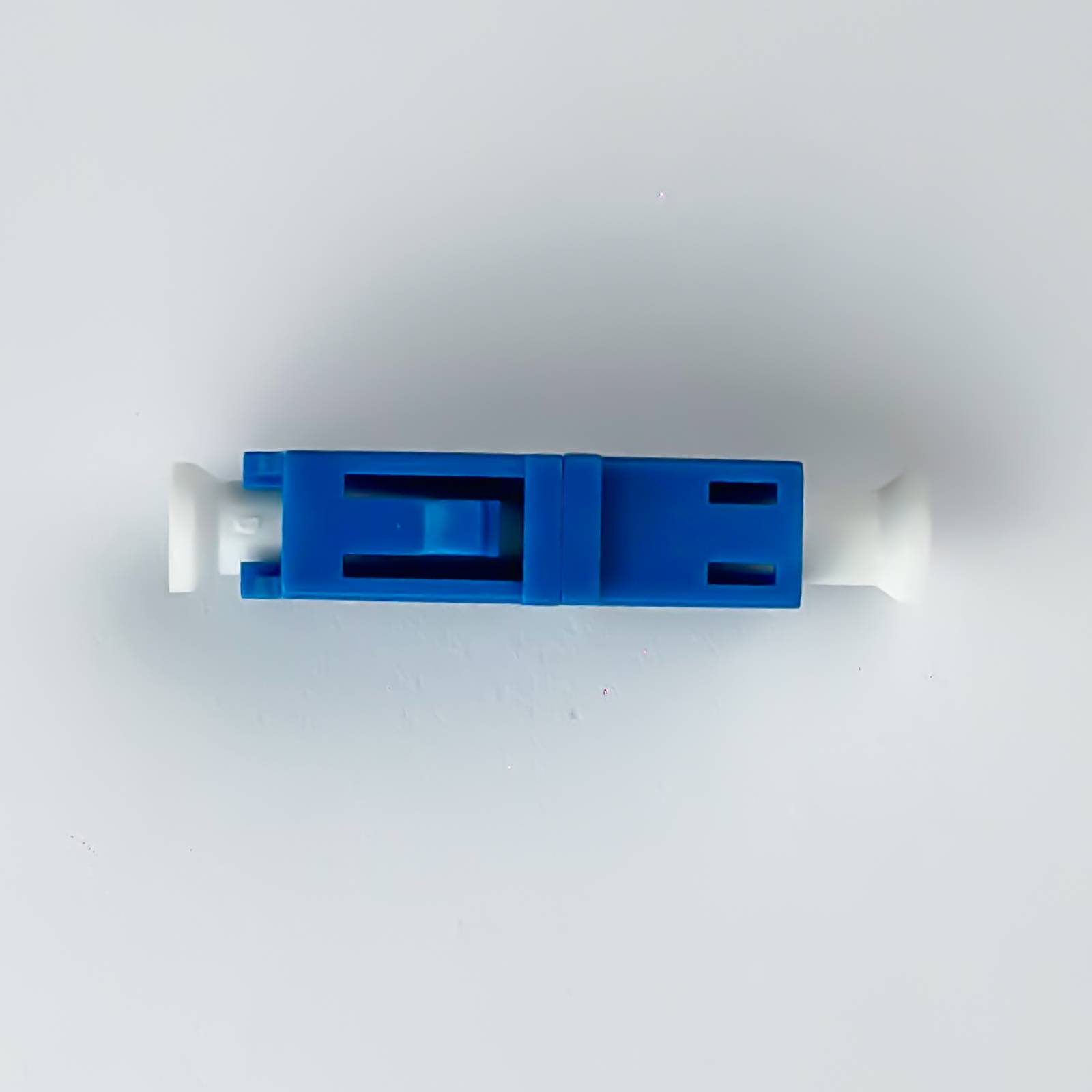 Blauer Kunststoff-Lichtwellenleiter-Adapterverbinder mit weißen Enden, zentriert auf einem einfachen, hellen Hintergrund dargestellt.