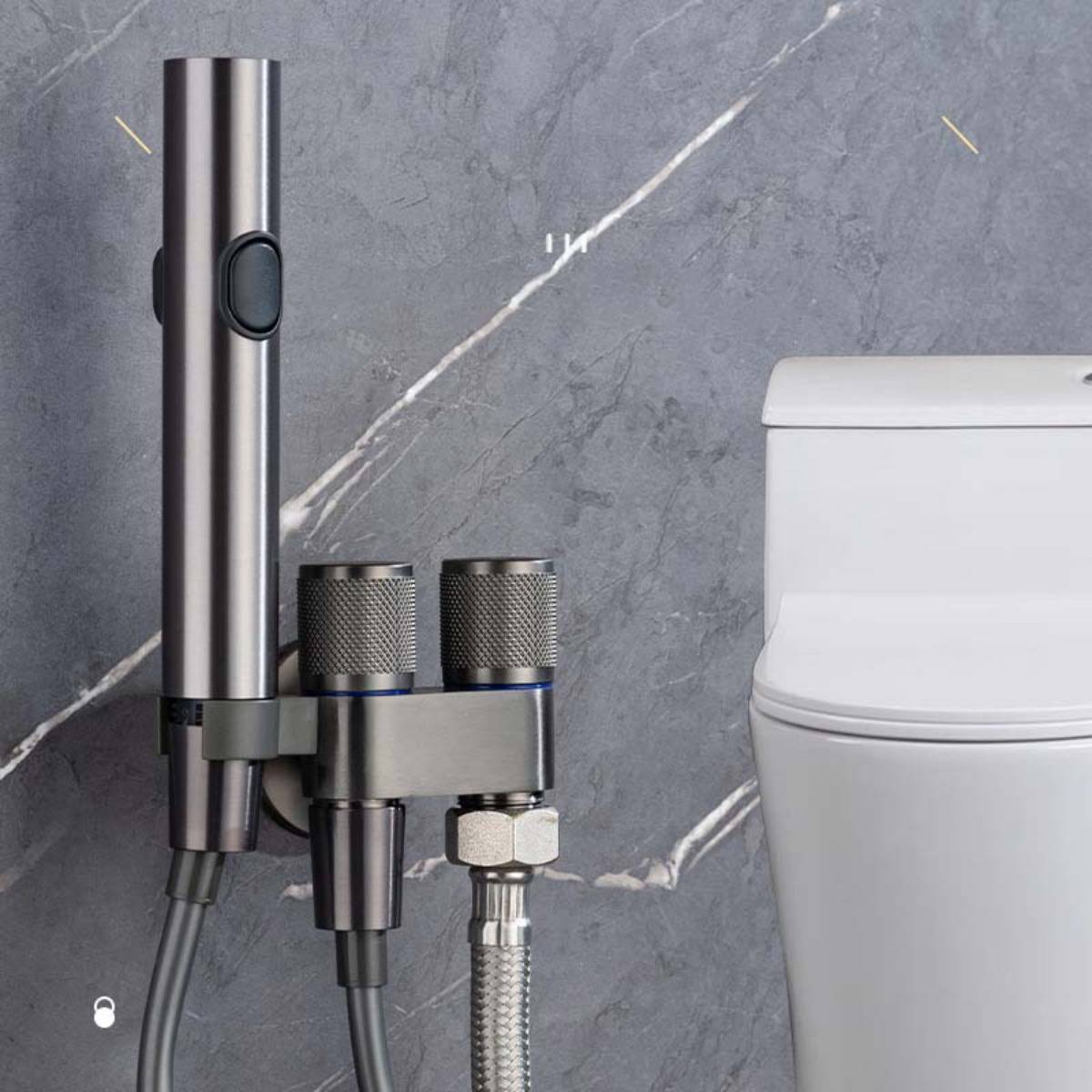 Edelstahl-Bidetspray und Dual-Kontrollventile, die neben einer weißen Toilette an einer grauen Fliesenwand montiert sind.