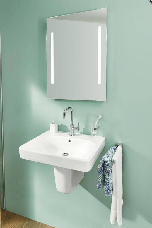 An der Wand montiertes Badezimmerbecken mit verchromtem Wasserhahn, Spiegelschrank, Zahnbürstenhalter und Handtuch an einer mintgrünen Wand.