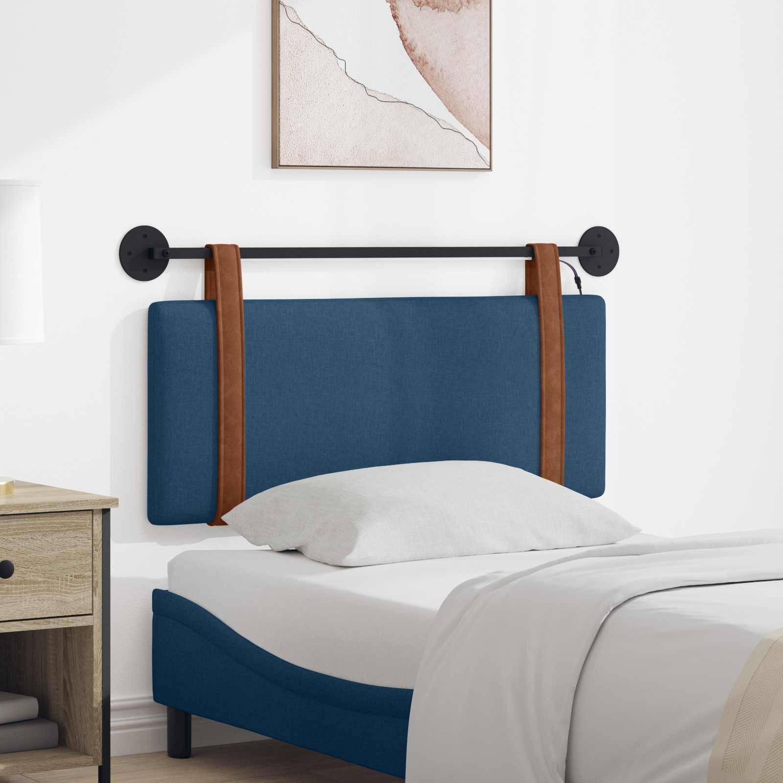 Kopfteil mit blauer Polsterung und braunen Riemen auf einem weißen Bett in einem modernen Schlafzimmer, mit einem gerahmten Wanddruck darüber und einem kleinen Nachttisch in der Nähe.