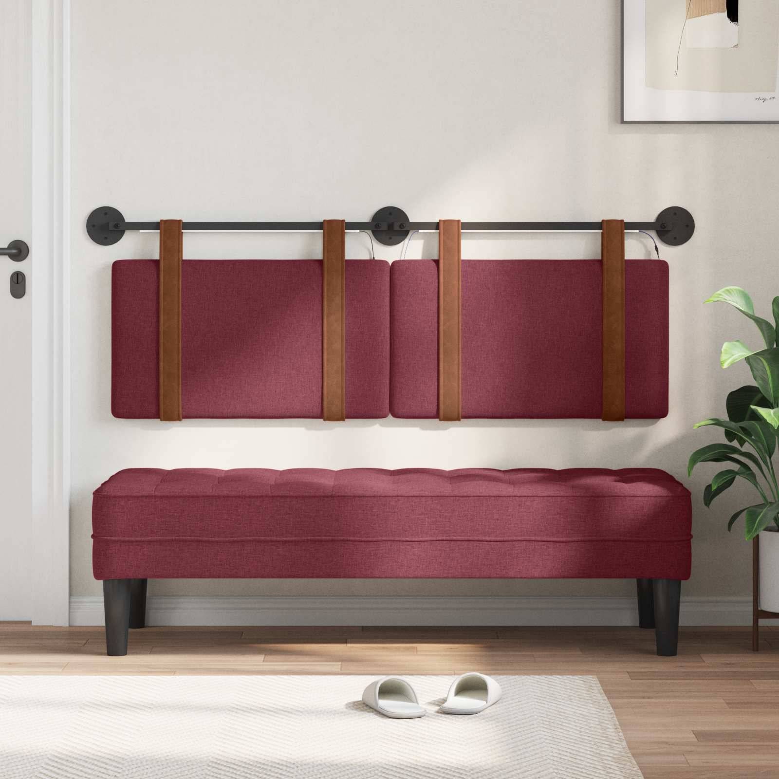 An der Wand montiertes burgunderrotes Klappsofa-Bänkchen mit braunen Riemen über einer passenden gepolsterten Bank in einem hellen Raum mit einer Pflanze und Hausschuhen.