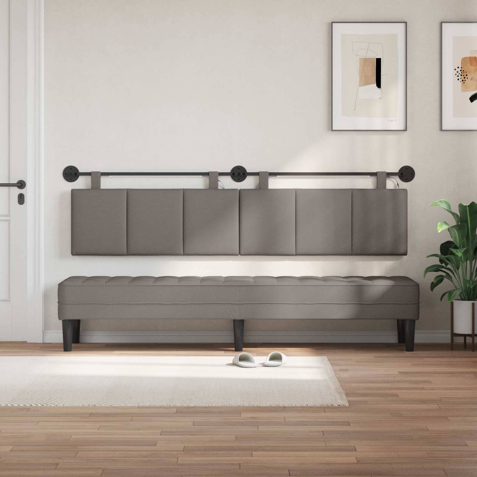 Ein minimalistisches Zimmer zeigt eine grau gepolsterte wandmontierte Bank mit einer passenden Bank darunter, gerahmte Kunst darüber, eine Pflanze rechts und Hausschuhe auf einem Teppich.