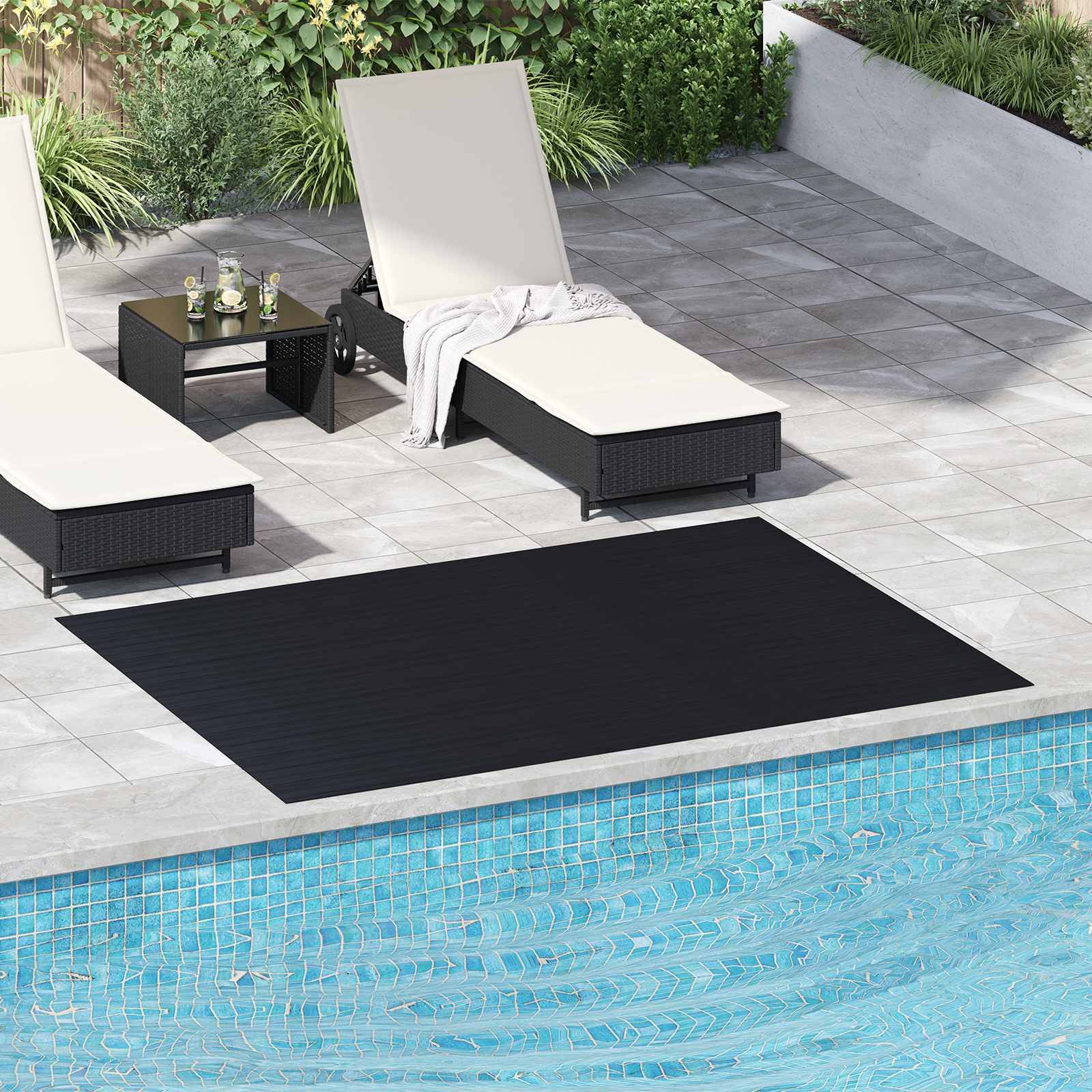 Zwei cremefarbene Chaiselongues und ein kleiner Tisch stehen auf einer gefliesten Pooldeck neben einem blauen Swimmingpool, mit einem schwarzen Outdoor-Teppich und Grünflächen in der Nähe.