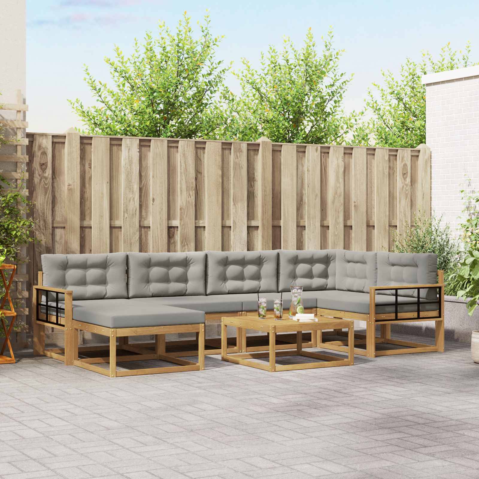Gartenmöbel-Set für die Terrasse mit grauen Kissen, Holzrahmen und einem niedrigen Couchtisch in einem eingezäunten Hinterhof.