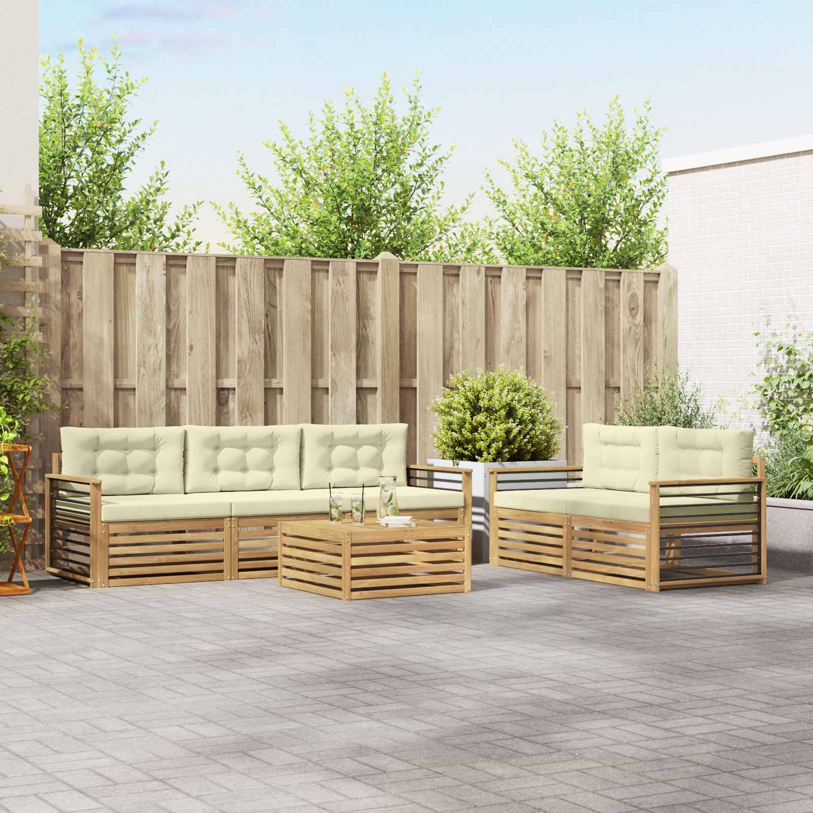 Outdoor-Terrassensitzgarnitur mit cremefarbenen Kissen, Holzlatten-Sofas, Couchtisch und Topfpflanzen vor einem Zaun.