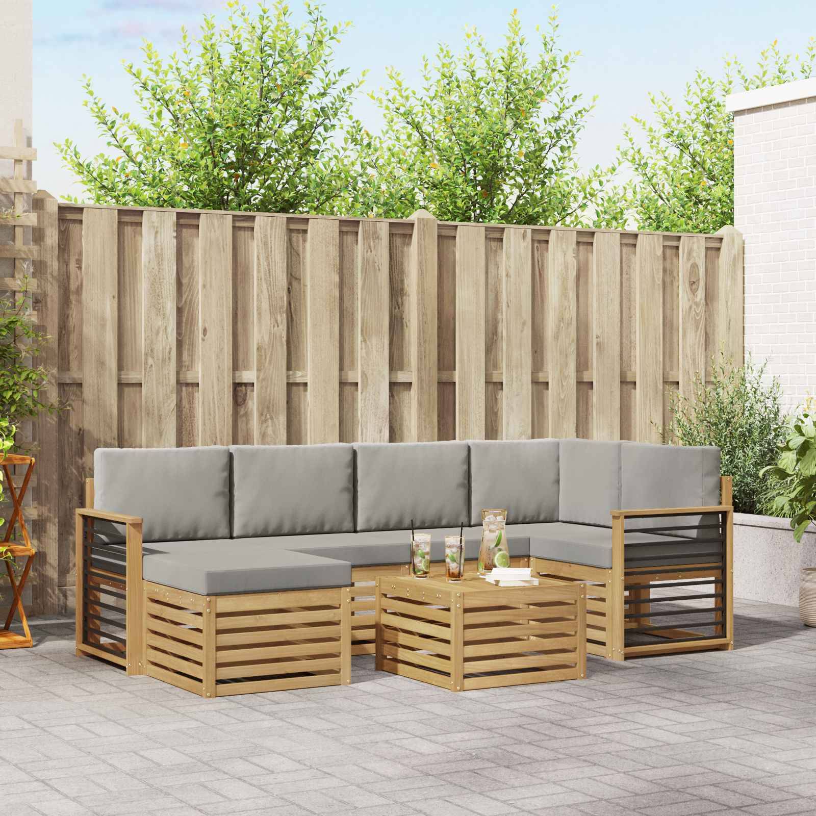 Outdoor-Terrassensitzgruppe mit grauen Kissen, Holzlatten-Rahmen und passenden Couchtischen vor einem eingezäunten Hinterhof.