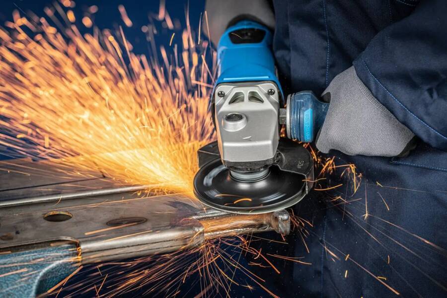 Handschuh tragender Arbeiter, der einen Winkelschleiffer auf Metall verwendet und dabei helle Funken beim Schneiden oder Schleifen erzeugt.