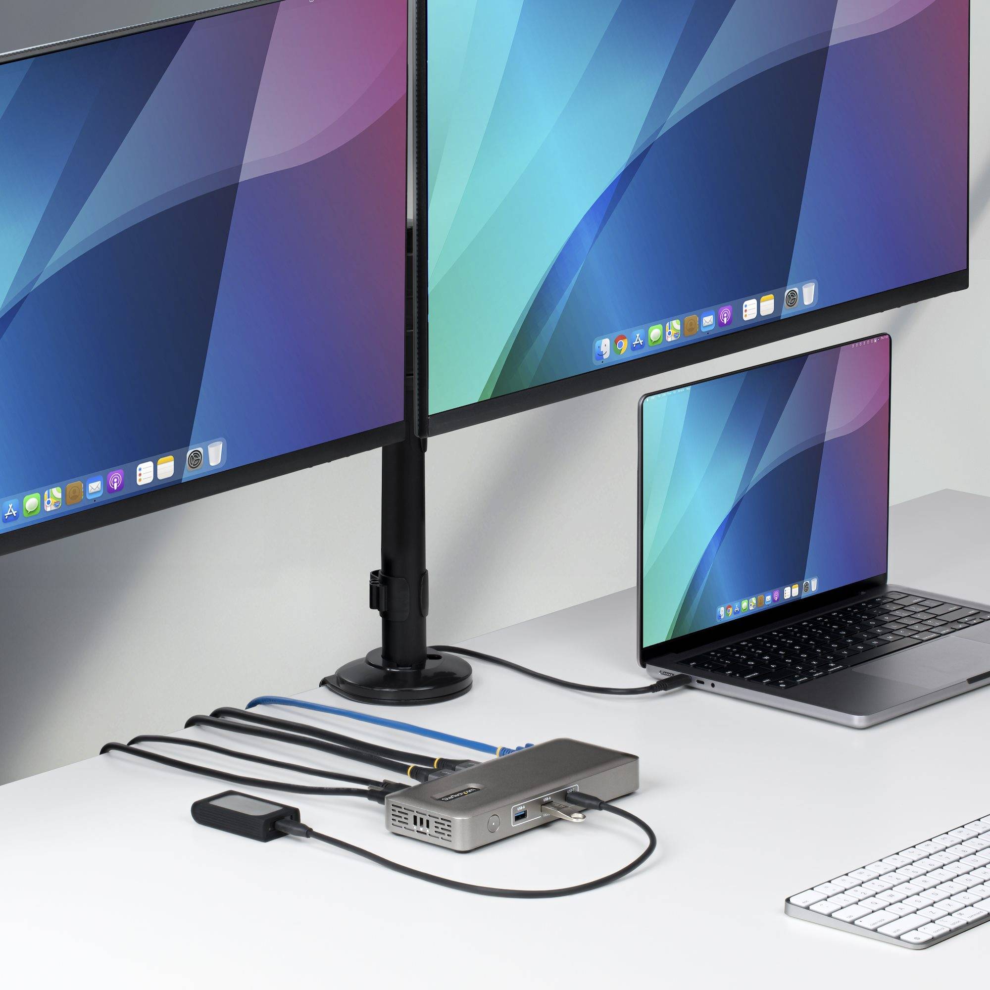 Laptop, der über ein kleines Dock auf einem Schreibtisch mit zwei externen Monitoren verbunden ist und eine Multi-Display-Workstation-Konfiguration zeigt.