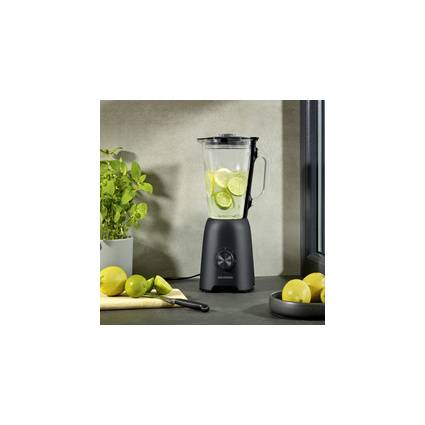 Mixer mit Limettenscheiben auf einer Küchenablage neben Zitronen, einem Messer und Basilikum, was auf die Zubereitung eines frischen Zitrusgetränks hindeutet.