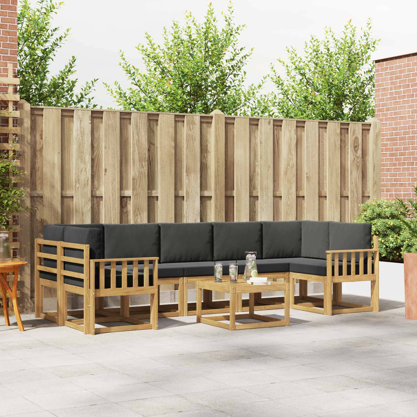Sitzmöbel-Set für die Terrasse im Freien mit schwarzen Kissen, Holzlehnstühlen und Couchtischen vor einem Gartenzaun-Hintergrund.