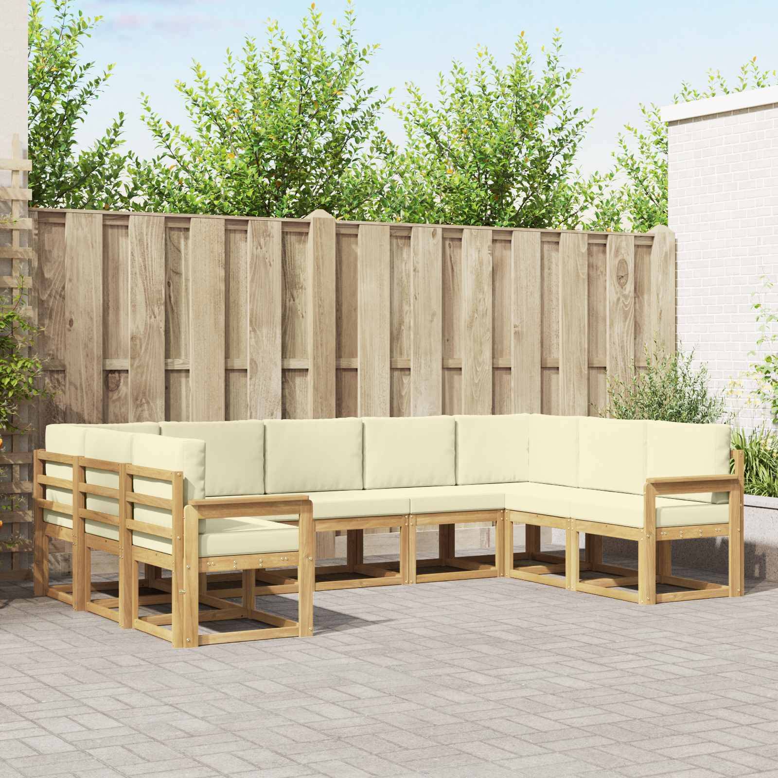 Außenterrasse mit hellem Holz-Ecksofa und cremefarbenen Kissen vor einem Holzzaun und Gartenbäumen.