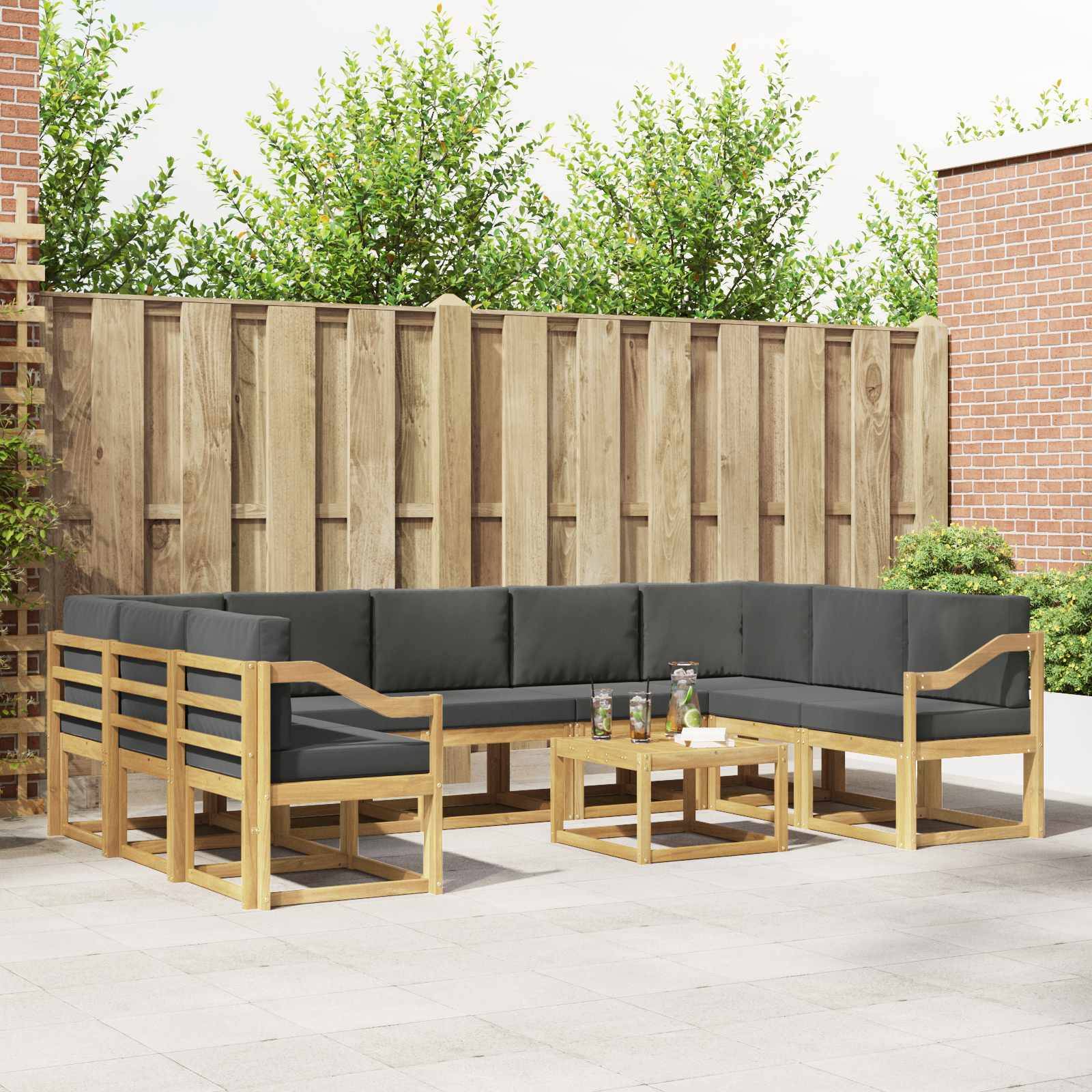 Gartenmöbel-Set für die Terrasse mit Lounge-Sofa mit Holzrahmen und passenden Couchtischen auf einer gepflasterten Terrasse neben einem Zaun