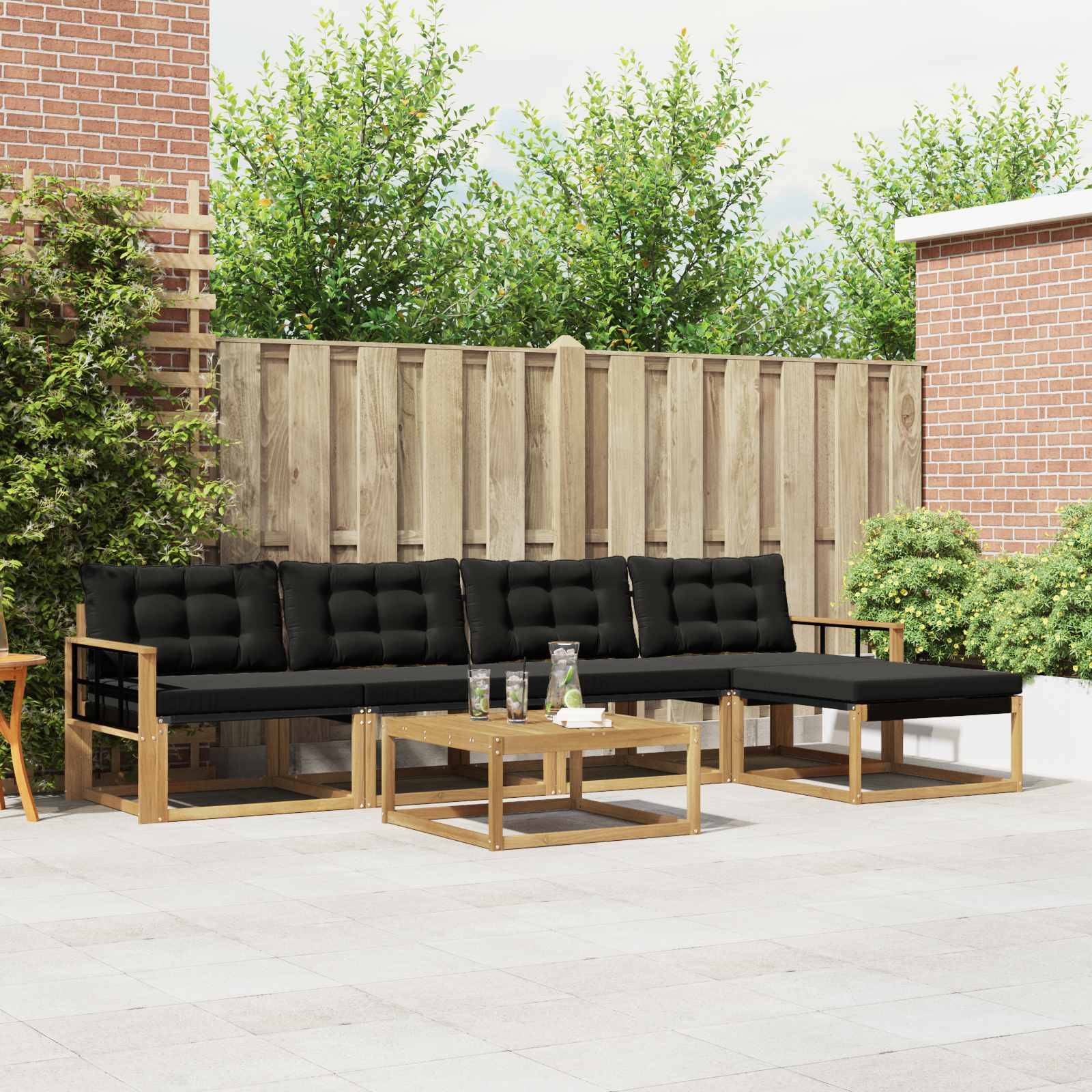 Außenterrasse mit schwarzem, gepolstertem Ecksofa mit Holzrahmen und Couchtischen an einem Zaun und Backsteinmauern.