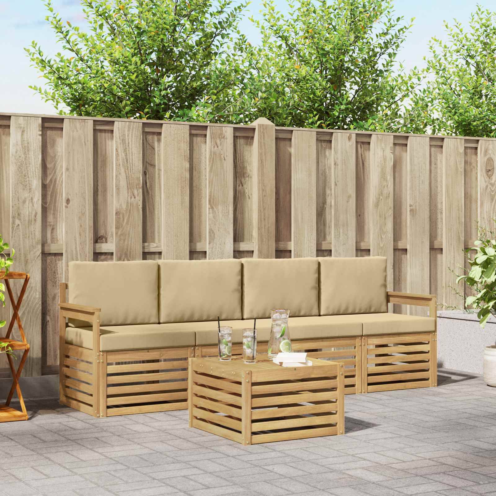 Sitzmöbel für die Terrasse im Freien mit beigen Kissen, hölzernem Sofa und Couchtisch auf grauem Belag vor einem Holzzaun.