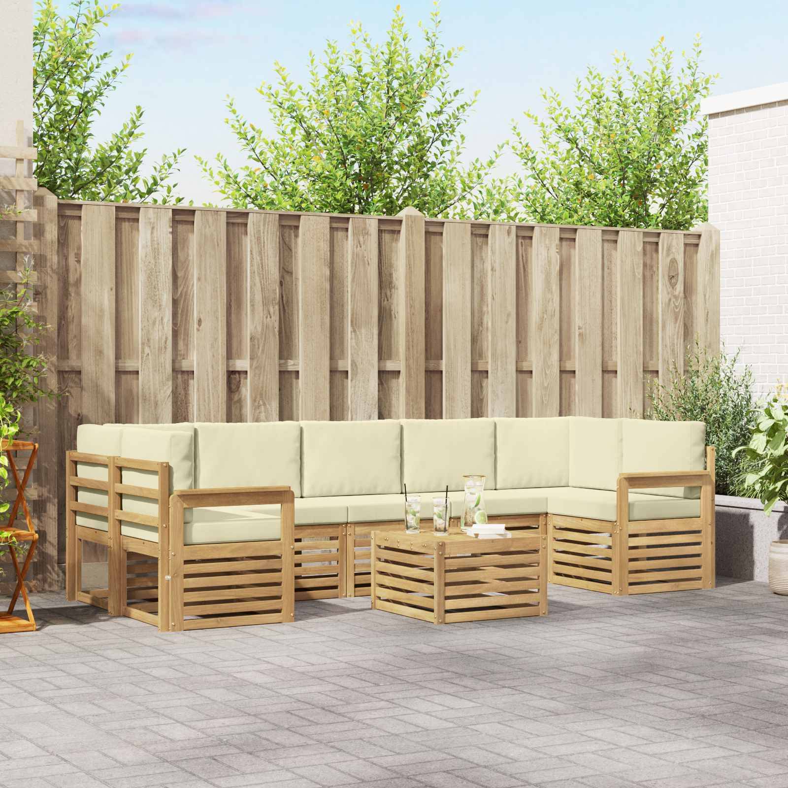 Outdoor-Patio mit einem hellholzfarbenen, L-förmigen Ecksofa, passendem Couchtisch und cremefarbenen Kissen in einem umzäunten Hinterhof.