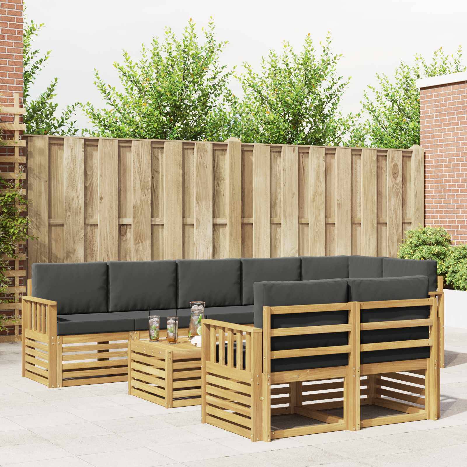 Outdoor-Terrassensitzgruppe mit graugepolsterten Holz-Ecksofa und passendem Couchtisch in einem eingezäunten Hinterhof.