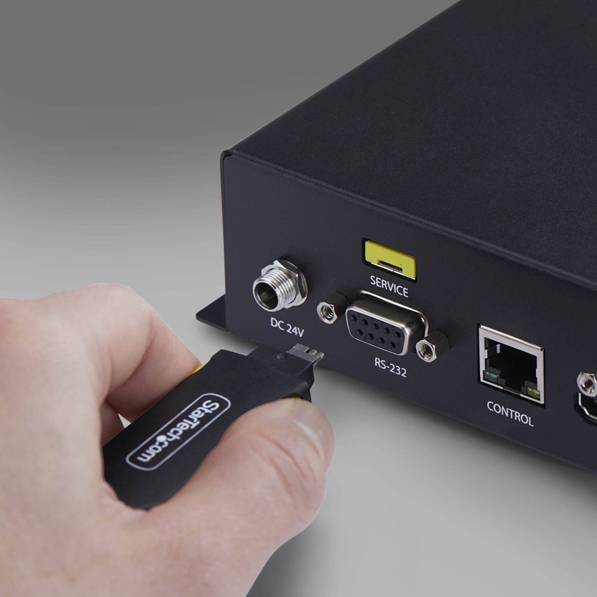 Hand steckt ein SanDisk USB-Stick in die DC 24V Seite eines schwarzen elektronischen Geräts mit 