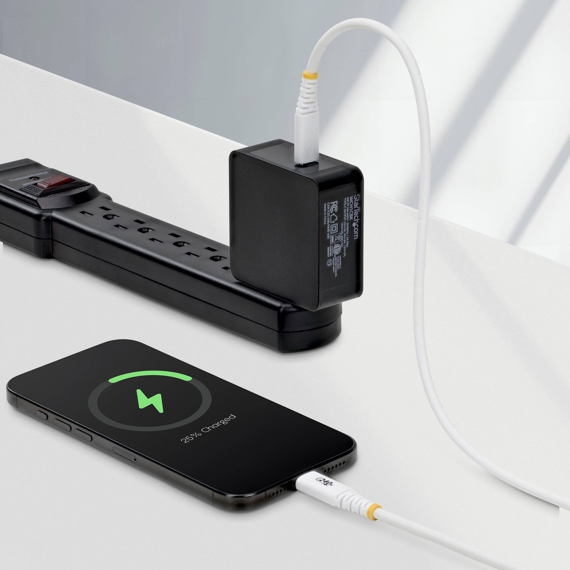 Smartphone-Aufladung per Kabel neben einer Steckdosenleiste mit eingestecktem Netzteil.