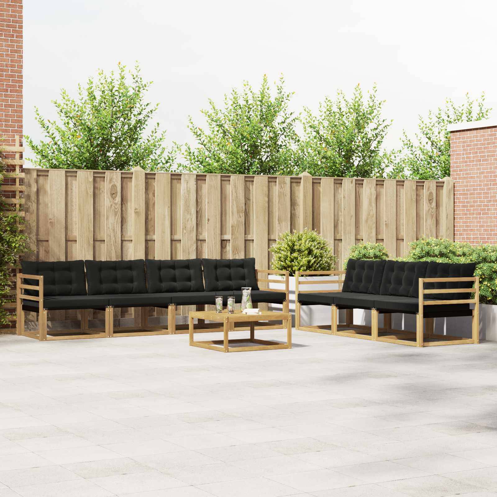 Outdoor-Terrassenbereich mit zwei schwarzgepolsterten Holzsofas, einem glastisch, Topfpflanzen und einem Holzzaun im Hintergrund.