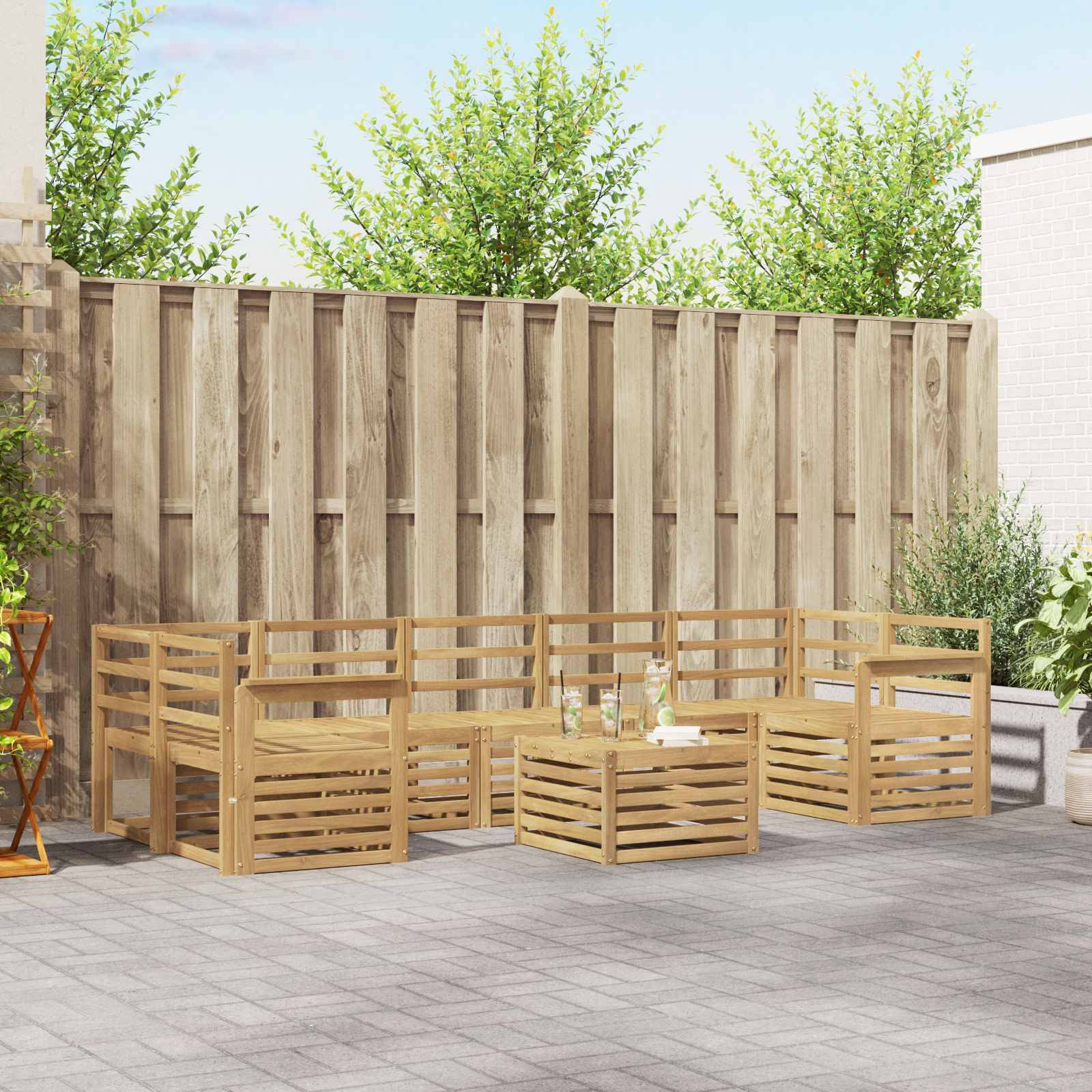 Outdoor-Terrasse mit hölzernem Ecksofa, passenden Tischen und einem kleinen Set aus Flasche und Gläsern vor einem hohen hölzernen Sichtschutzzaun.
