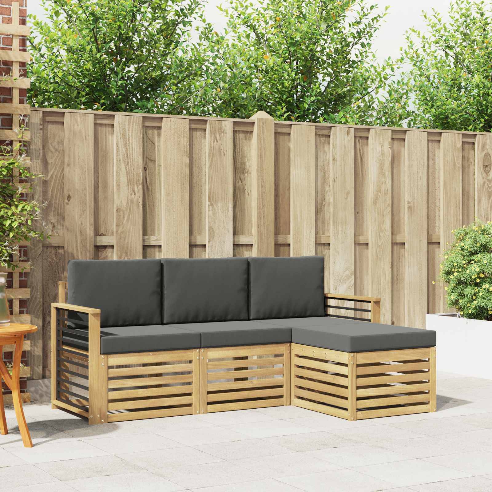 Außenterrassen-Ecksofa mit schwarzen Kissen und Holzlattenrahmen, vor einem Holzzaun und Grünflächen aufgestellt.