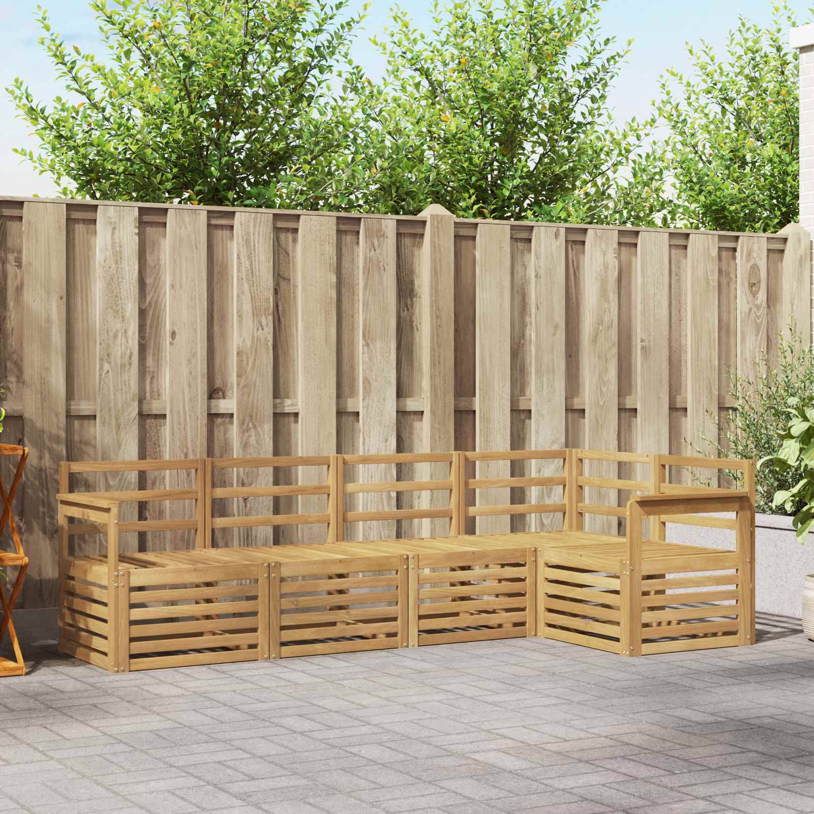 L-förmige Holzgartenbank mit Lamellenseiten auf einer gepflasterten Terrasse vor einem hohen Holzzaun und Bäumen.