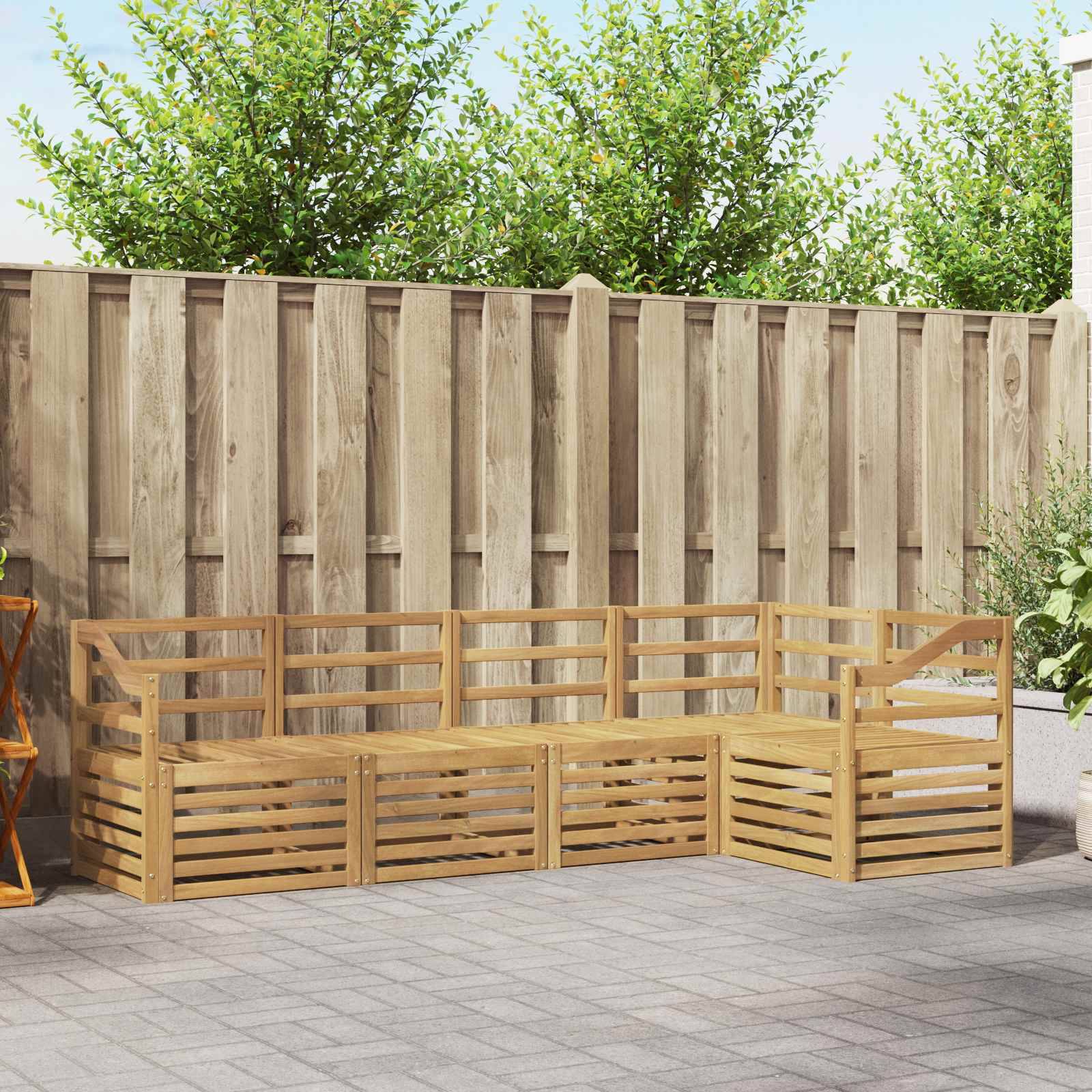 Holzgartenbank mit Eckform und Lamellensitz sowie Rückenlehne auf einem gepflasterten Patio neben einem hohen Zaun, mit Bäumen und Blumenkübeln dahinter.