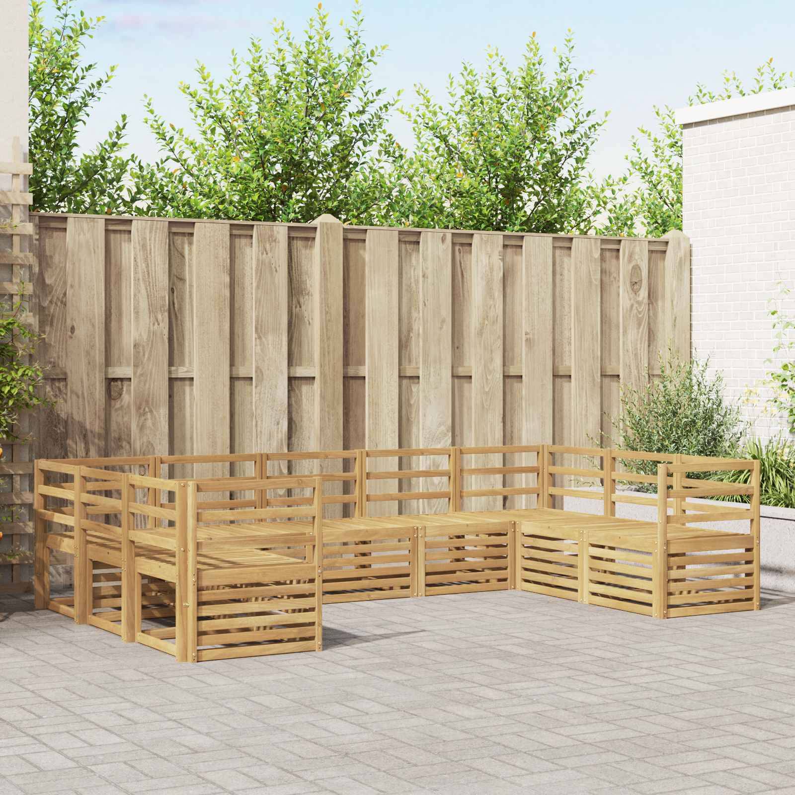 Modular Holzgarnitur für den Außenbereich in U-Form auf einer gepflasterten Terrasse neben einem hohen Zaun und Sträuchern.