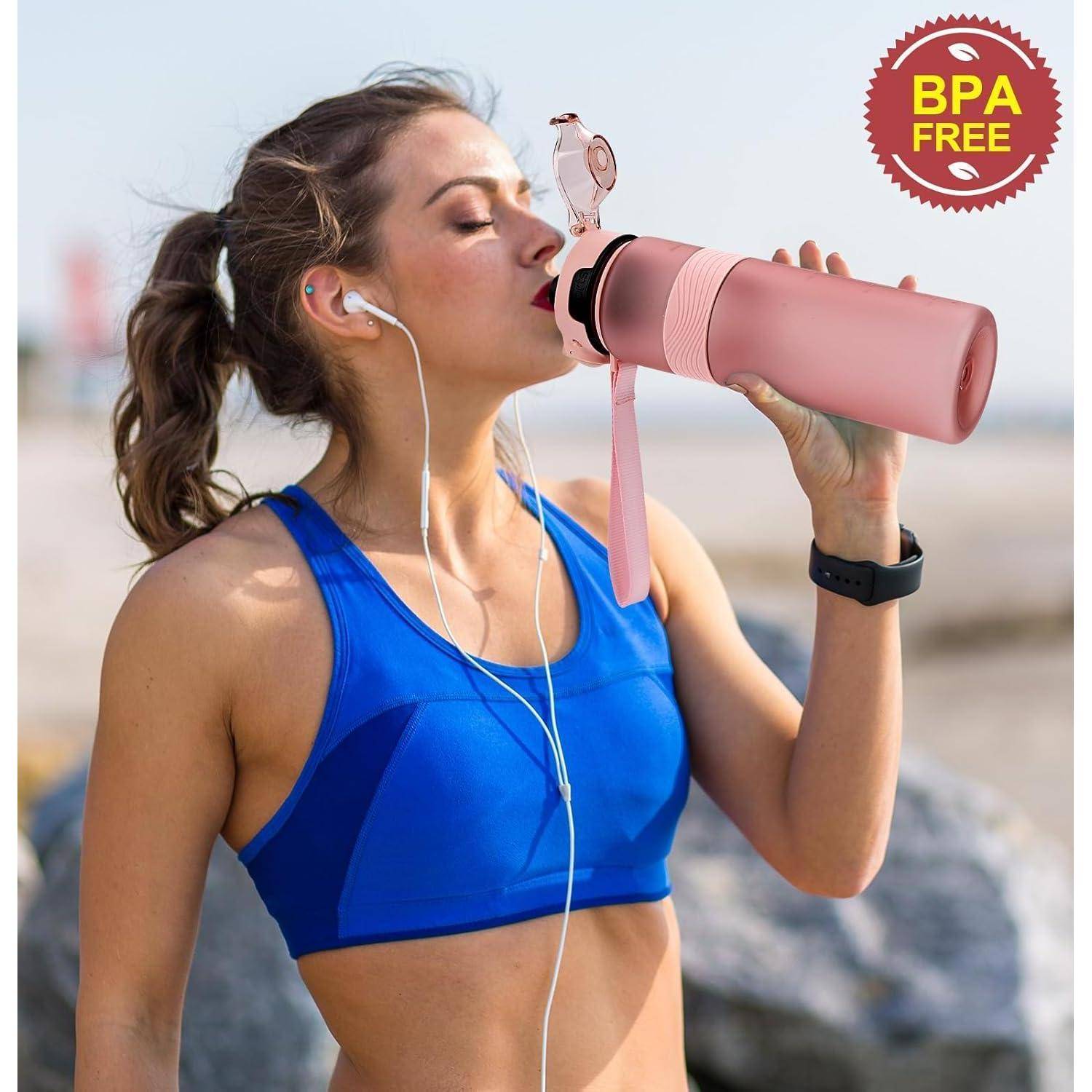 Eine Frau in einem blauen Sportoberteil trinkt aus einer rosa BPA-freien Wasserflasche, während sie draußen Kopfhörer trägt.