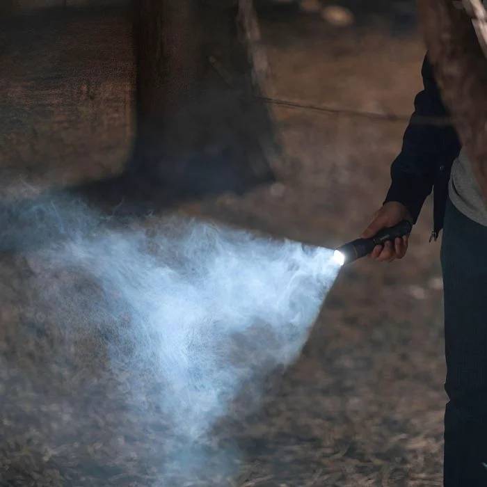 Person mit einer Taschenlampe, deren Strahl durch dichten Nebel oder Rauch in einer dunklen Außenumgebung scheint.
