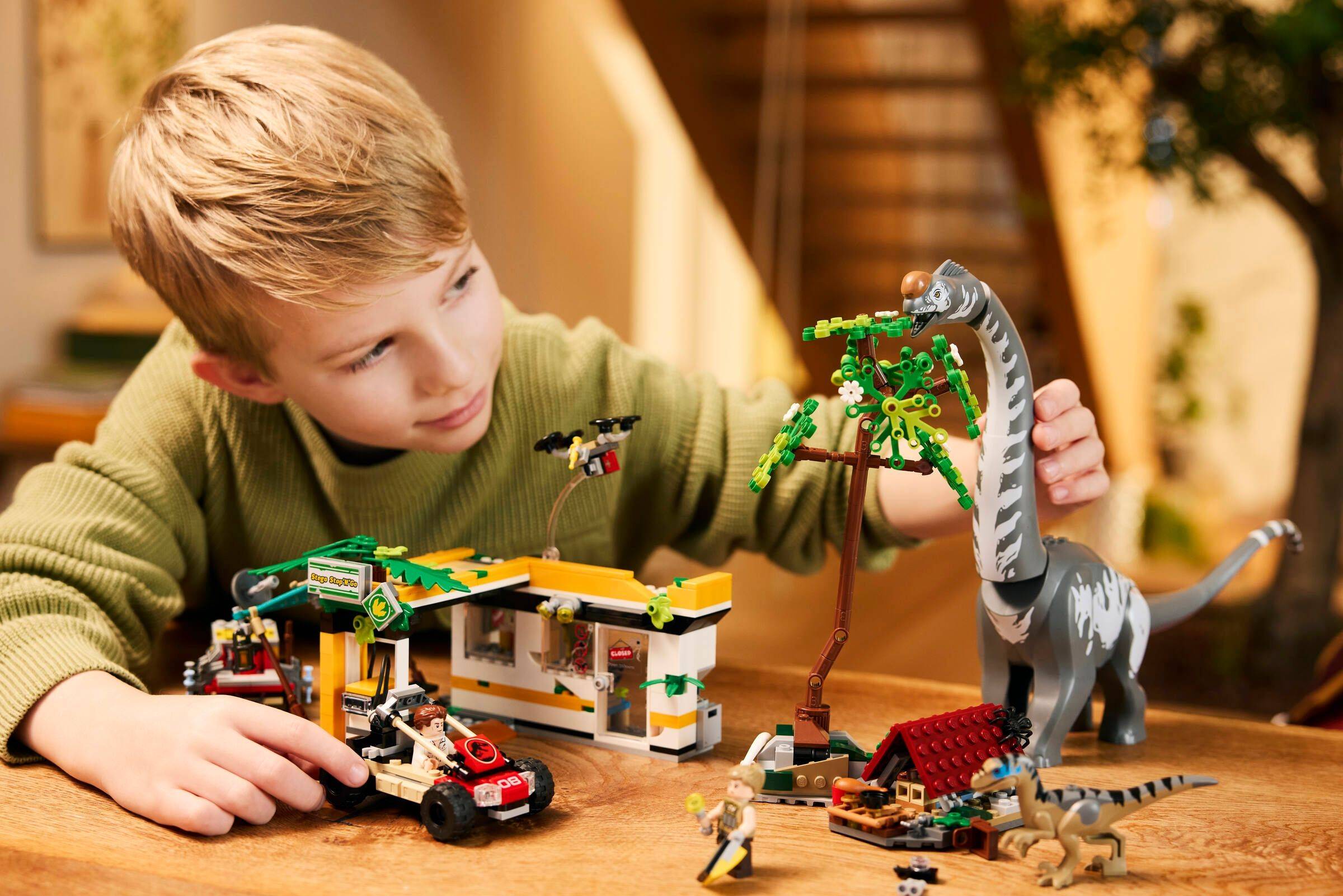 Junger Junge, der mit einem LEGO-Dinosaurier-Set und einem kleinen Spielzeuganuto auf einem Tisch im Innenbereich spielt.