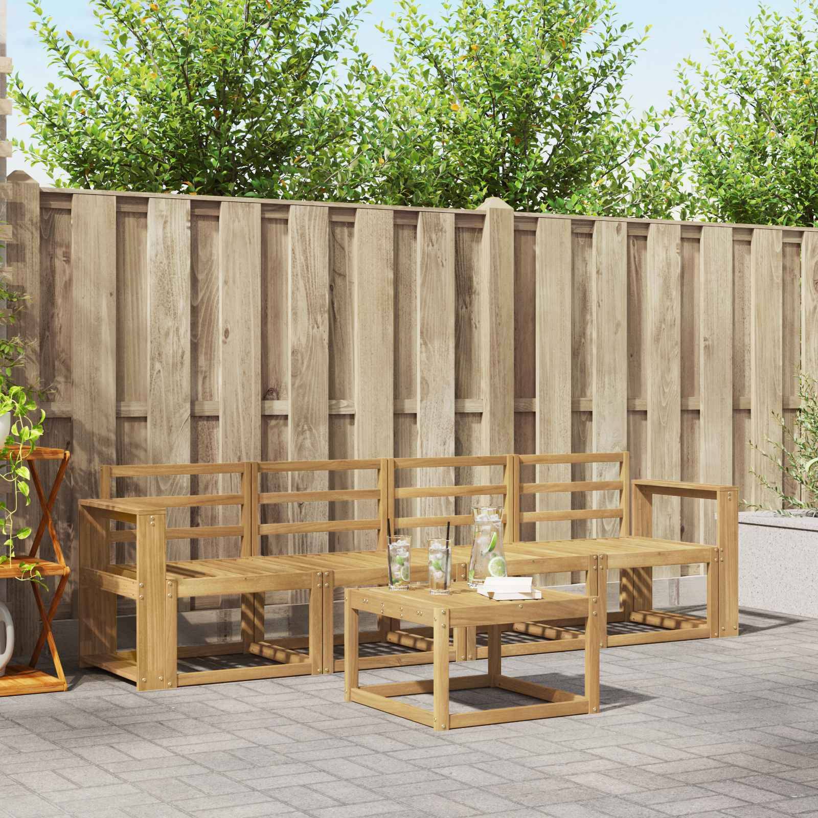 Sitzbereich auf der Außenterrasse mit einem Holzbanksatz und einem niedrigen Couchtisch auf einer gepflasterten Terrasse neben einem hohen Holzzaun und Grünanlagen.