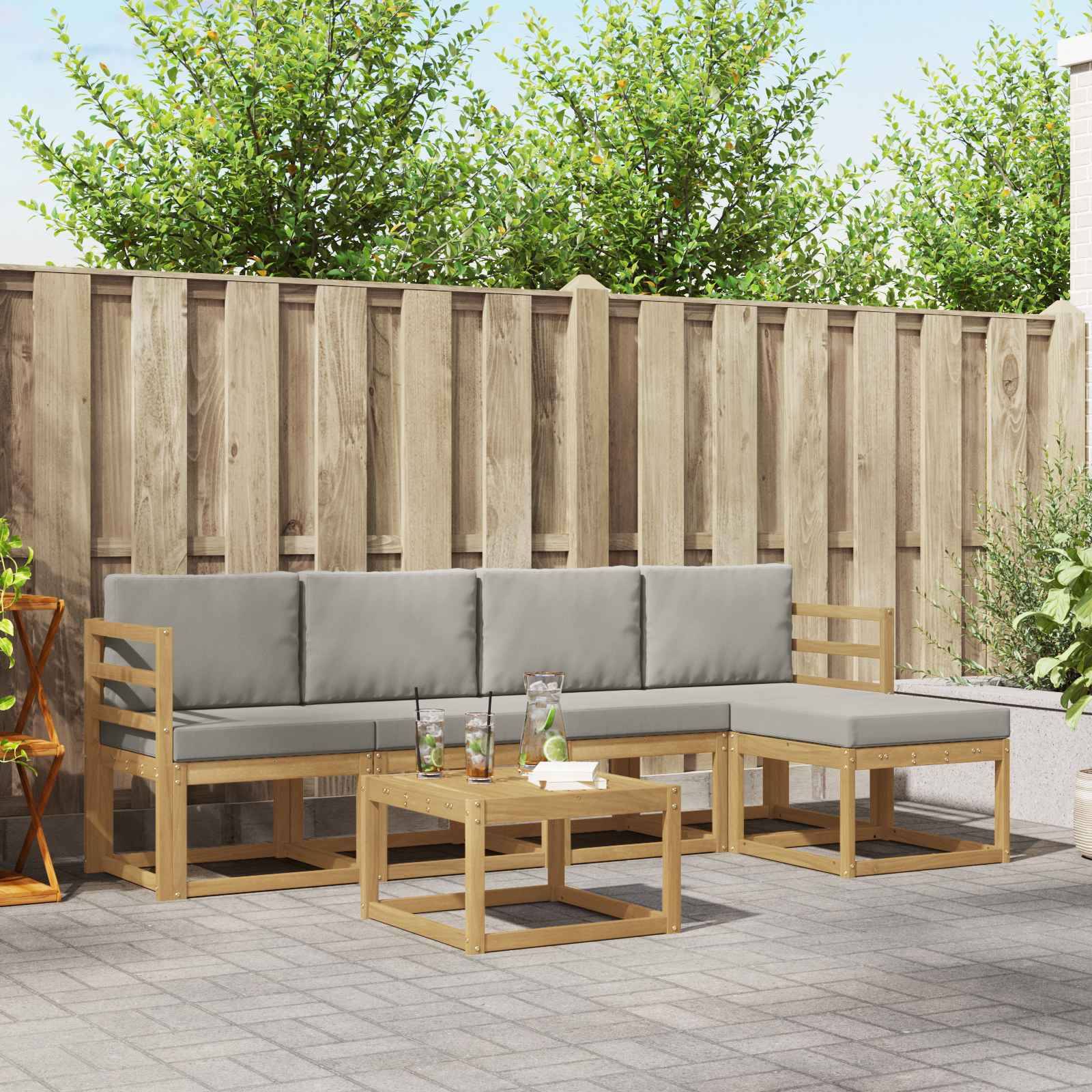 Gartenpolster-Set im Freien mit grauen Kissen, einem hölzernen Ecksofa und einem passenden Couchtisch vor einem Holzzaun.