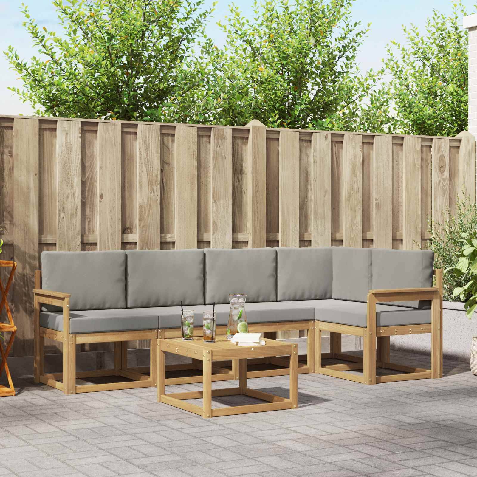 Outdoor-Terrassenbestuhlung mit grauen Kissen und Holzrahmen, die um einen niedrigen Couchtisch herum vor einem Holzzaun angeordnet sind.