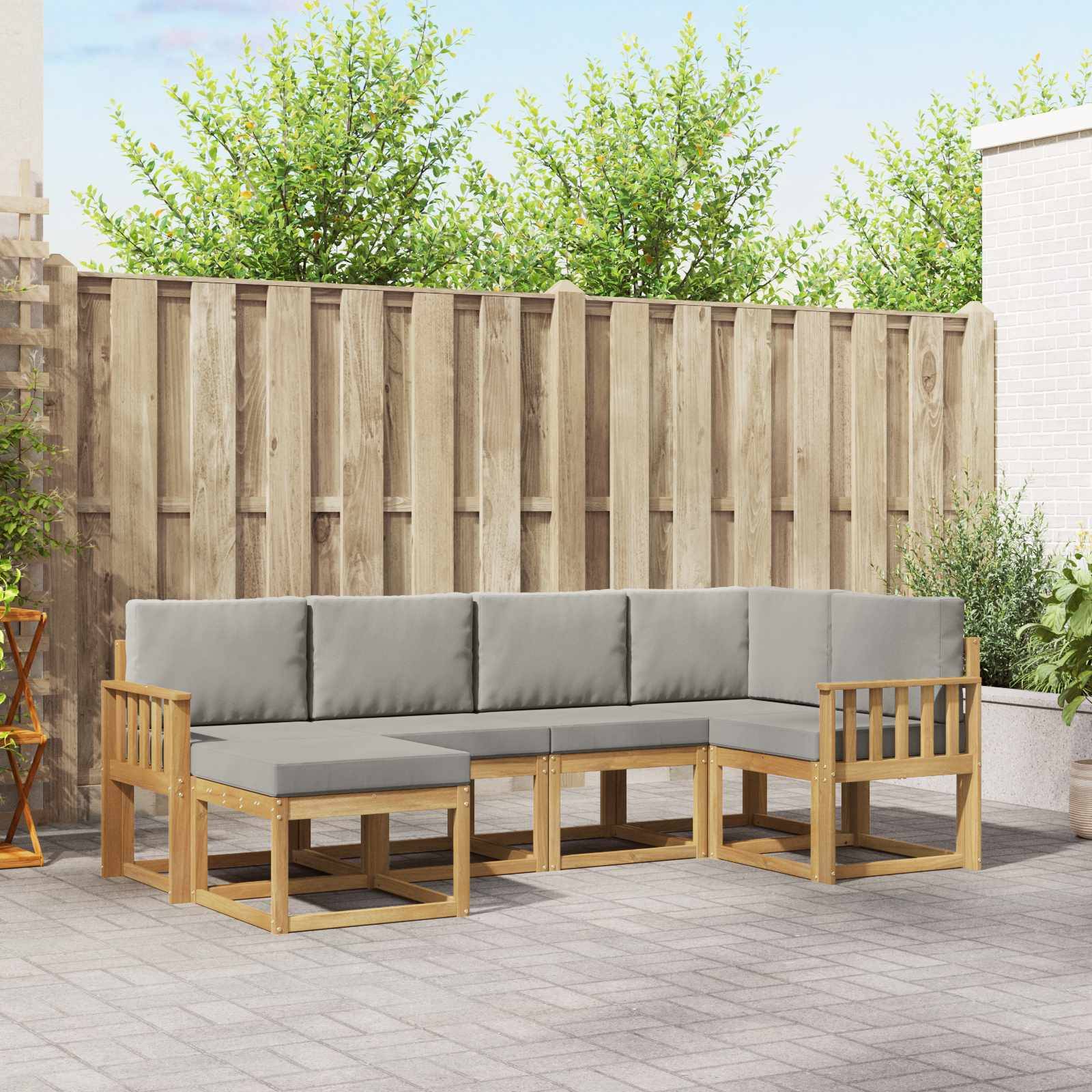 Outdoor-L-förmiges Holzsofa mit grauen Kissen auf einer Terrasse, vor einem Holzzaun und Grün.
