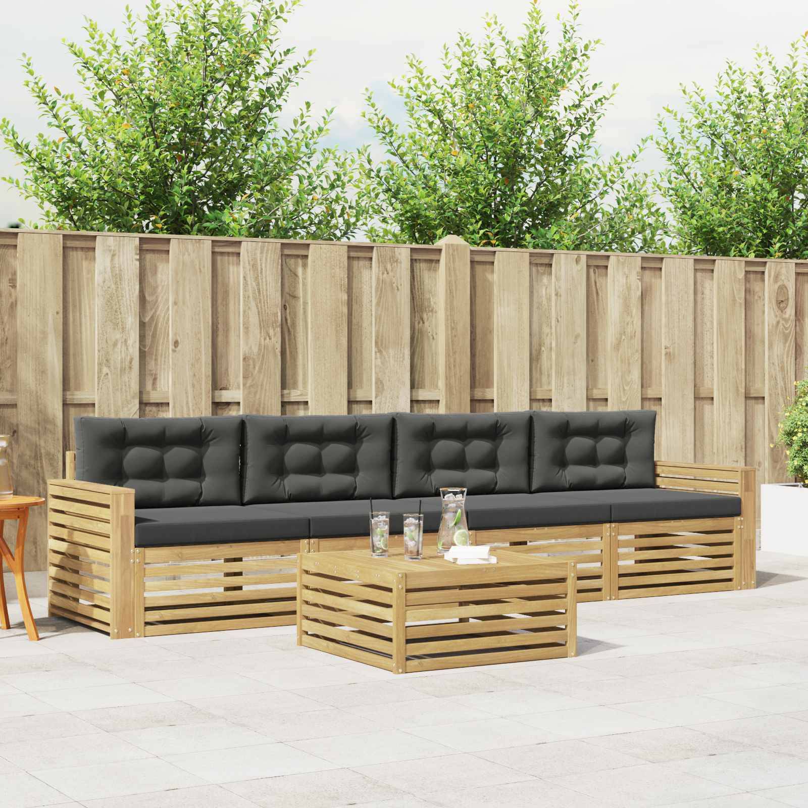 Sitzgruppe für die Außenterrasse mit schwarzem gepolstertem Holzsofa und passendem Couchtisch vor einem Holzzaun und Bäumen.